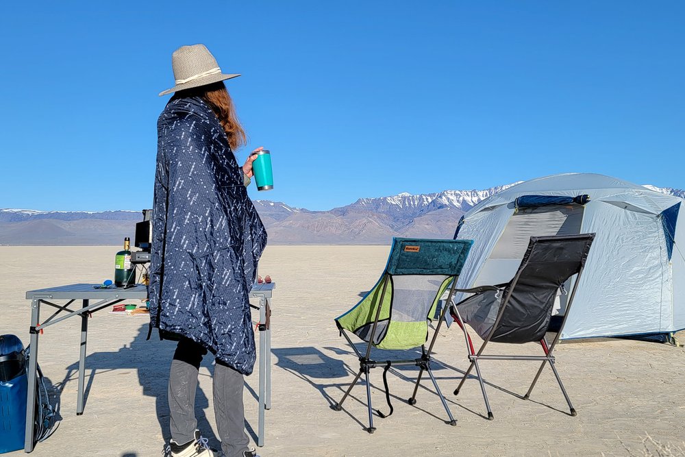 A person standing in a campsite in the desert wrapped up in a camp blanket