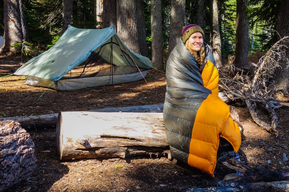 A hiker bundled up in a backpacking quilt at a campsite