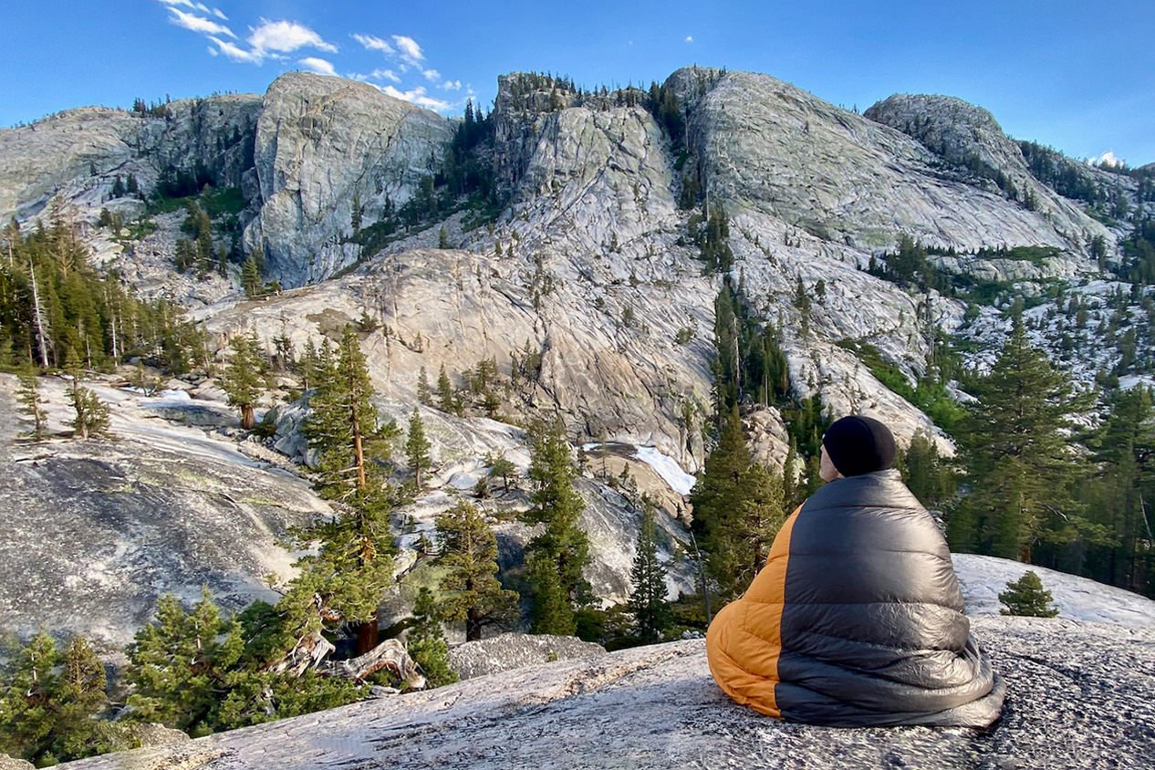 Hiker sitting with a quilt wrapped around them looking out on Yosemite National Park