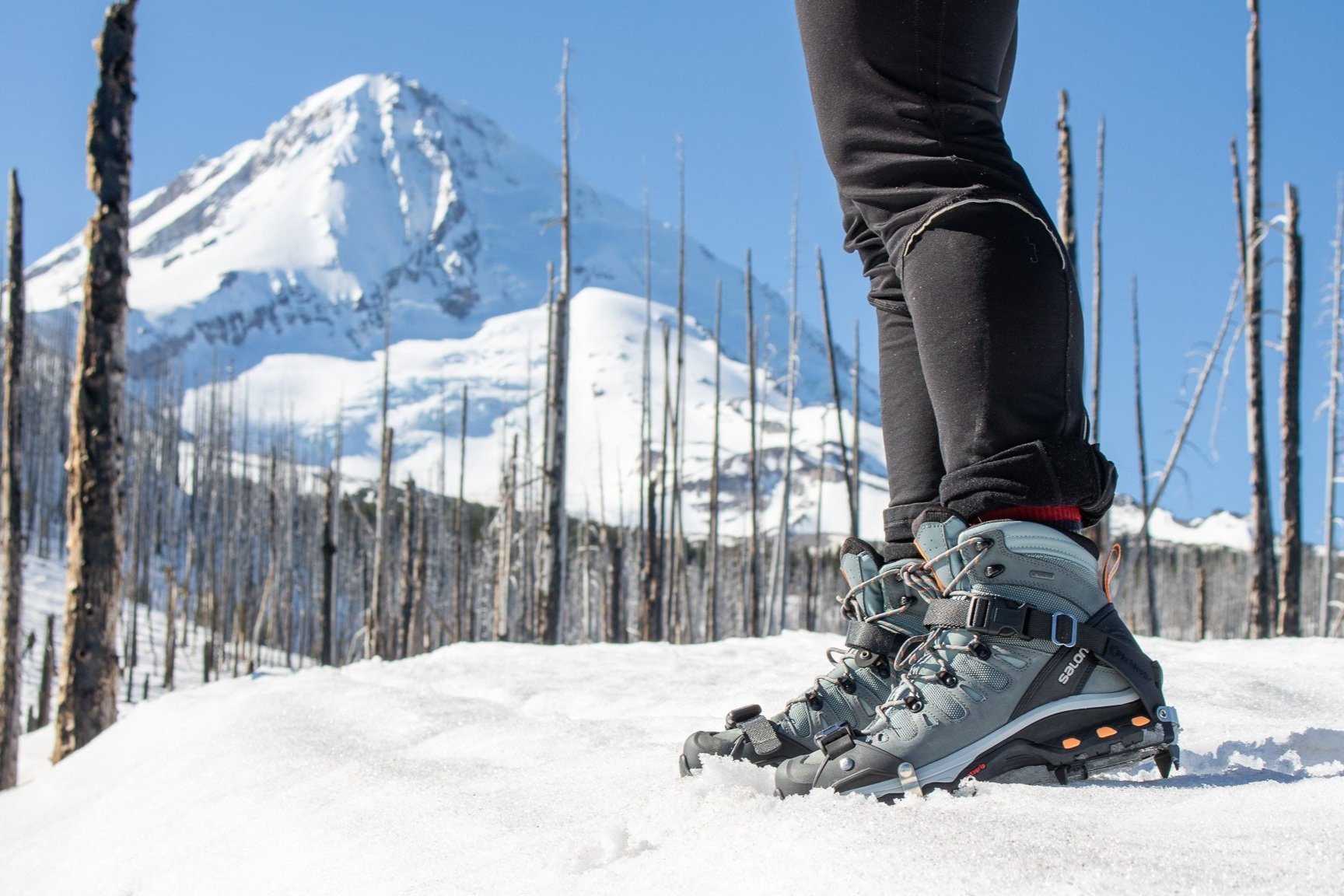 Closeup of the Salomon Quest 4 with traction devices in front of a snowy mountain