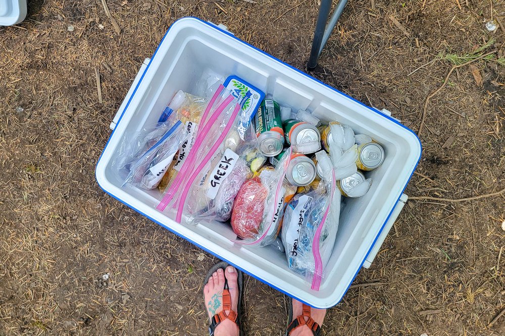 Top-down view of a cooler with labeled Ziploc bags filled with foil packet meal ingredients