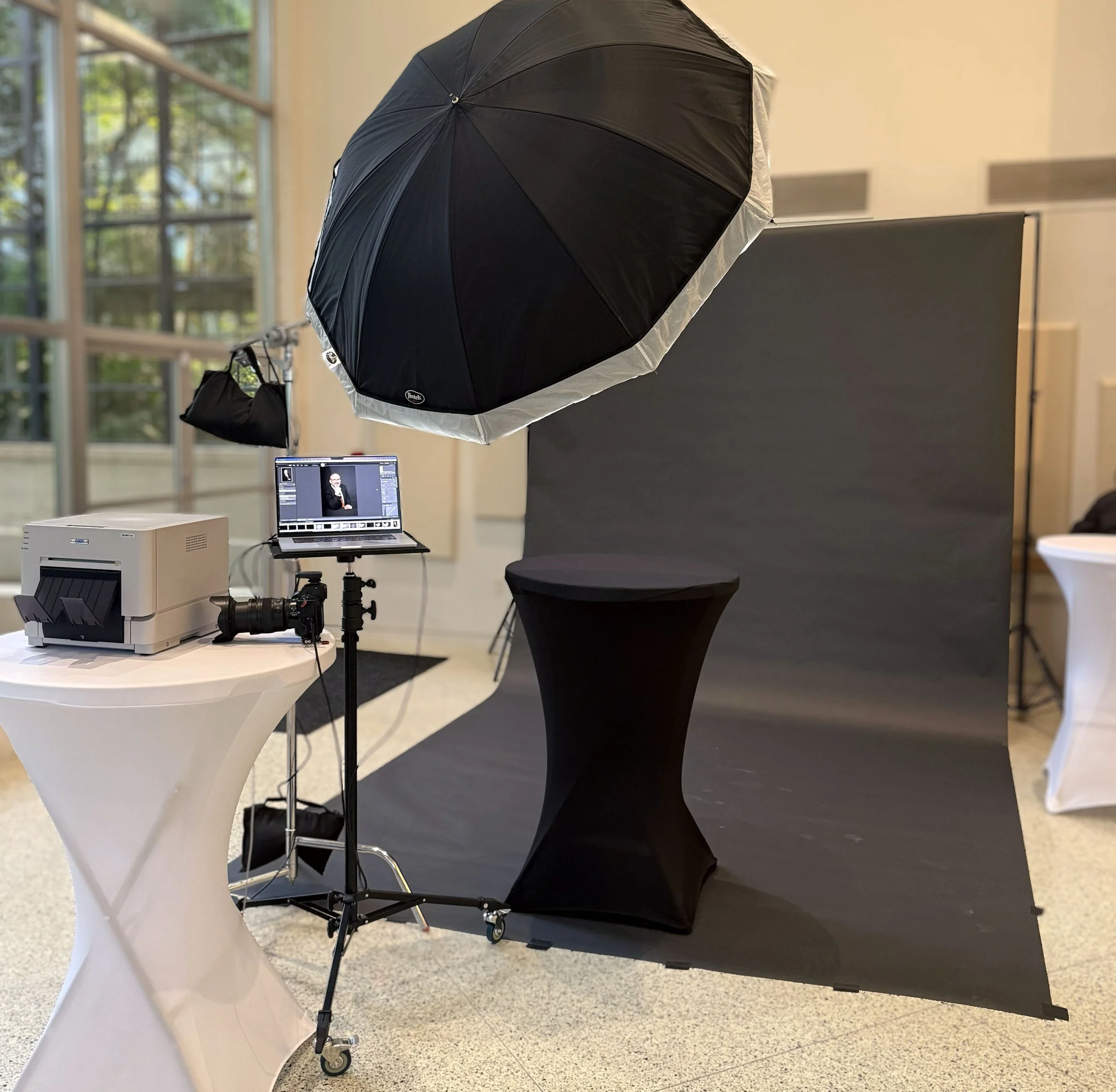 Wedding portrait booth setup showing photographer, lighting equipment, backdrop, and print station.