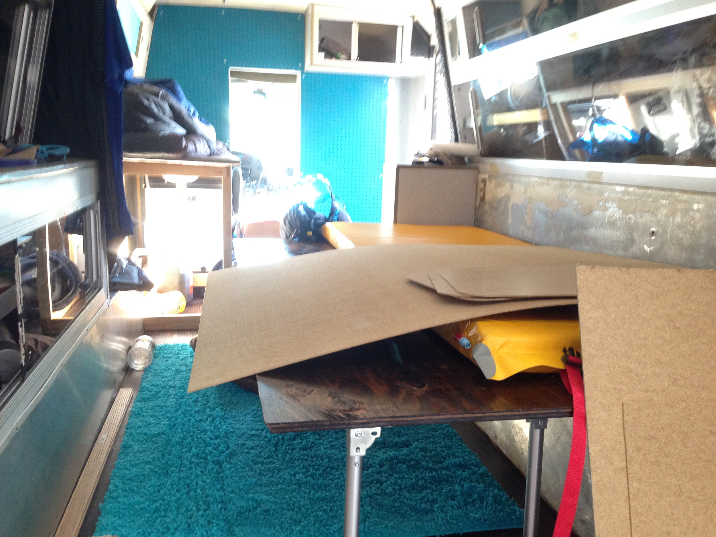 In this photo you can see the turquoise painted peg board we installed against the cab's rear wall, the basic kitchen framed out and the bed unfolded into its open position (slightly hidden underneath pressboard and a paco pad.)