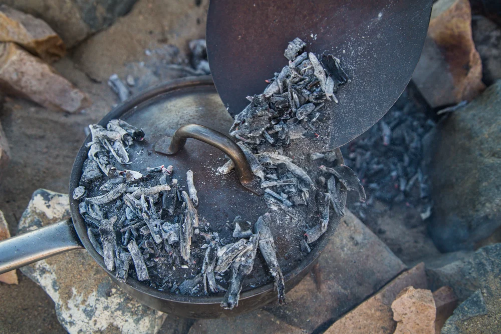 Piling coals on top of the dutch oven pan.
