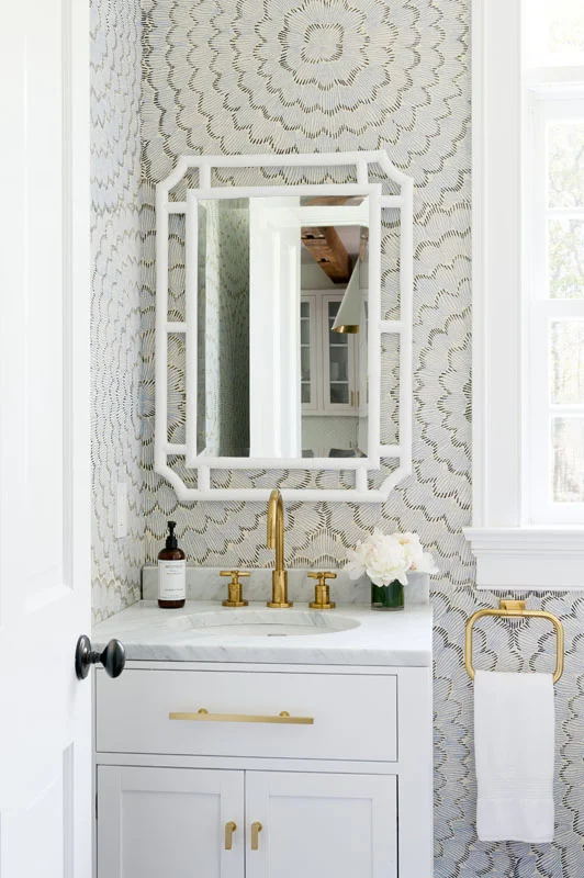 The powder room features antique brass accents and Celerie Kemble wallpaper that speak to both the youthfully modern and classically Hamptons styles that this home embodies.