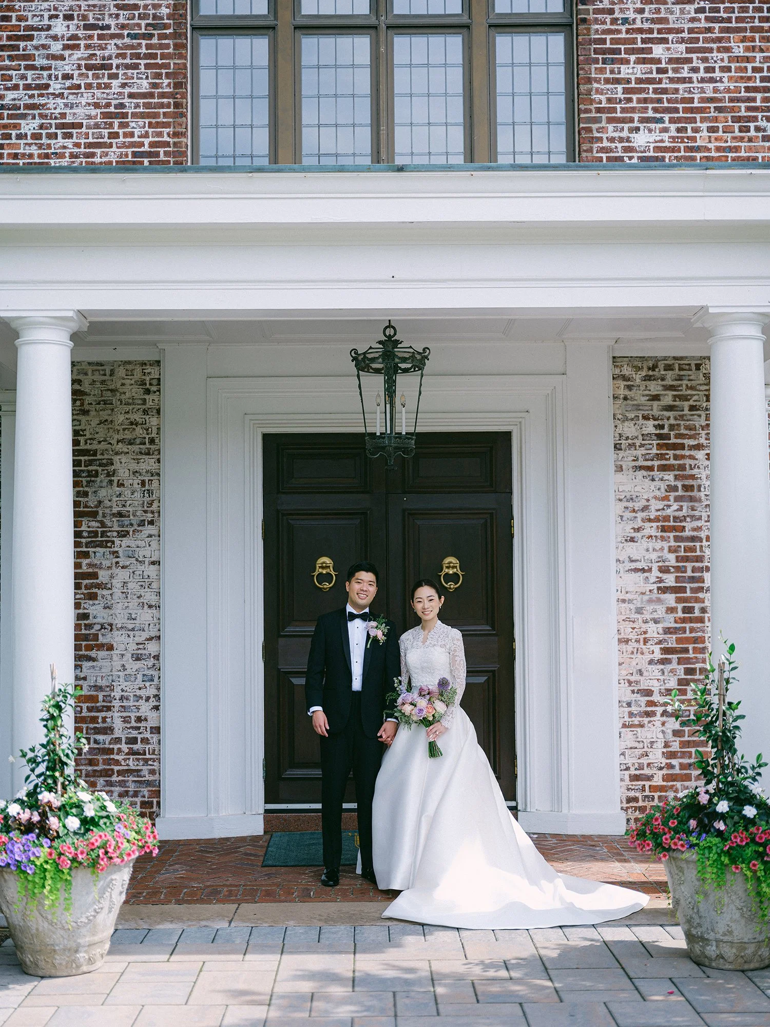 Wedding portrait of Amanda and Michael smiling in front of the historic mansion at Hamilton Farm Golf Club by Haseok Chung Studio.