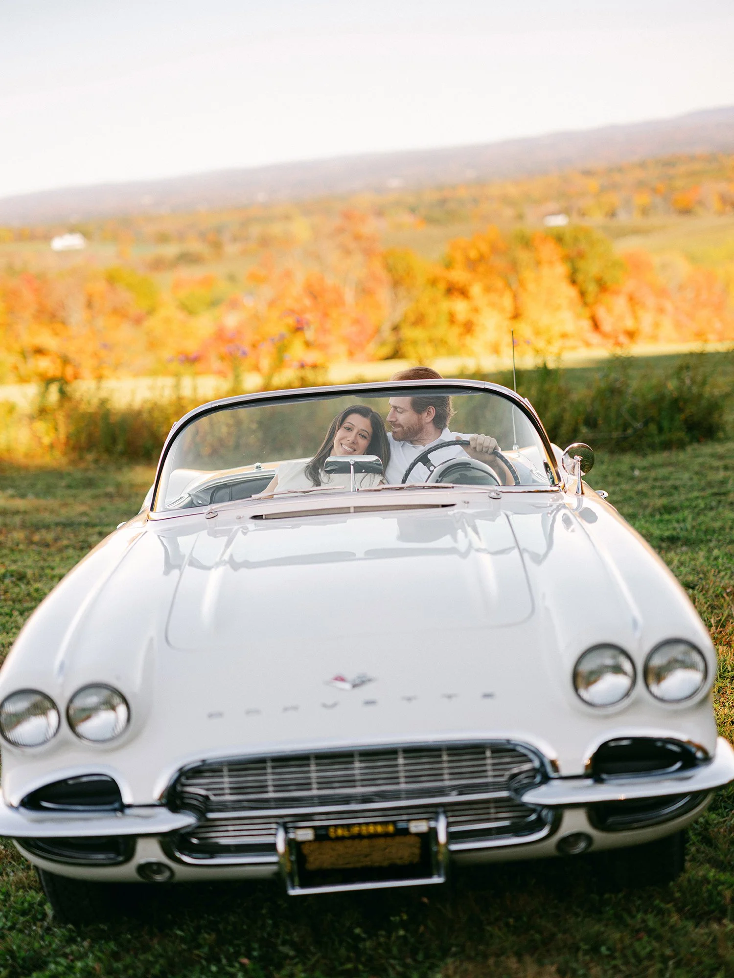 Daniel and Sandra beside a white 1960s Corvette convertible on a hill above the Hudson Valley