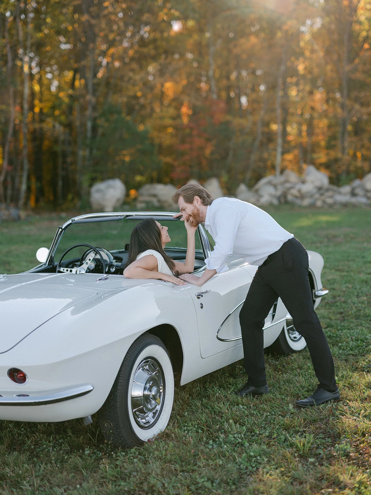 Daniel and Sandra beside a white 1960s Corvette convertible on a hill above the Hudson Valley
