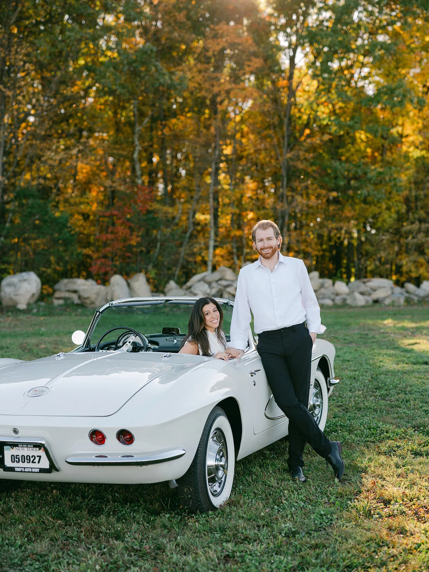 Daniel and Sandra beside a white 1960s Corvette convertible on a hill above the Hudson Valley