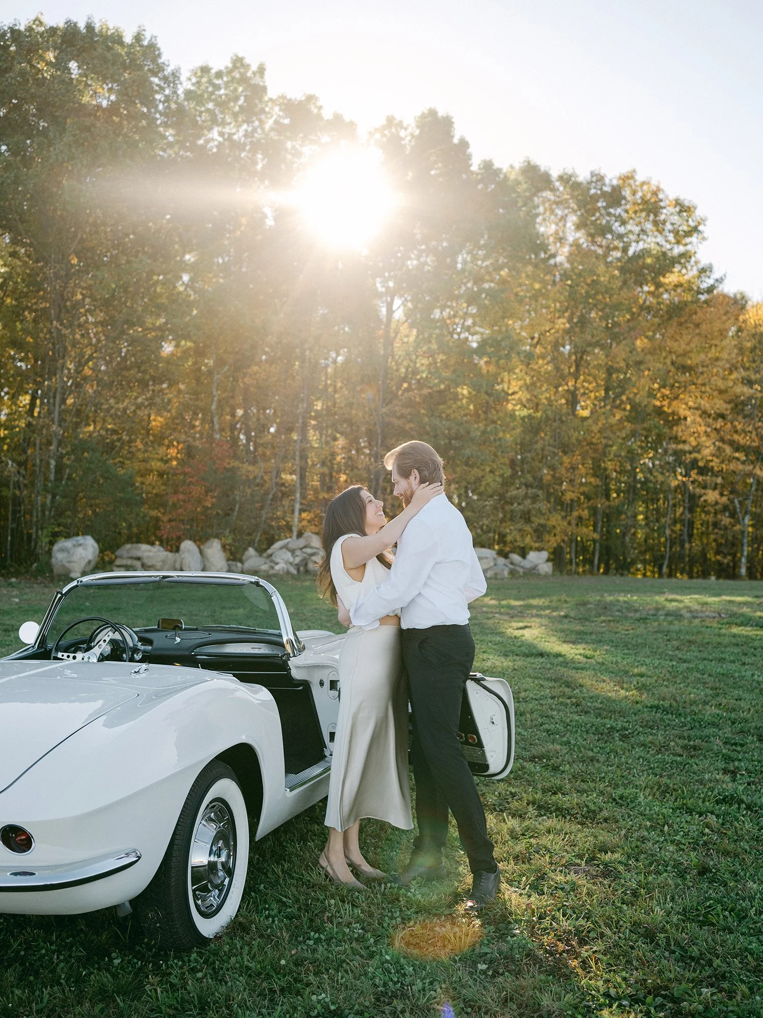 Daniel and Sandra beside a white 1960s Corvette convertible on a hill above the Hudson Valley