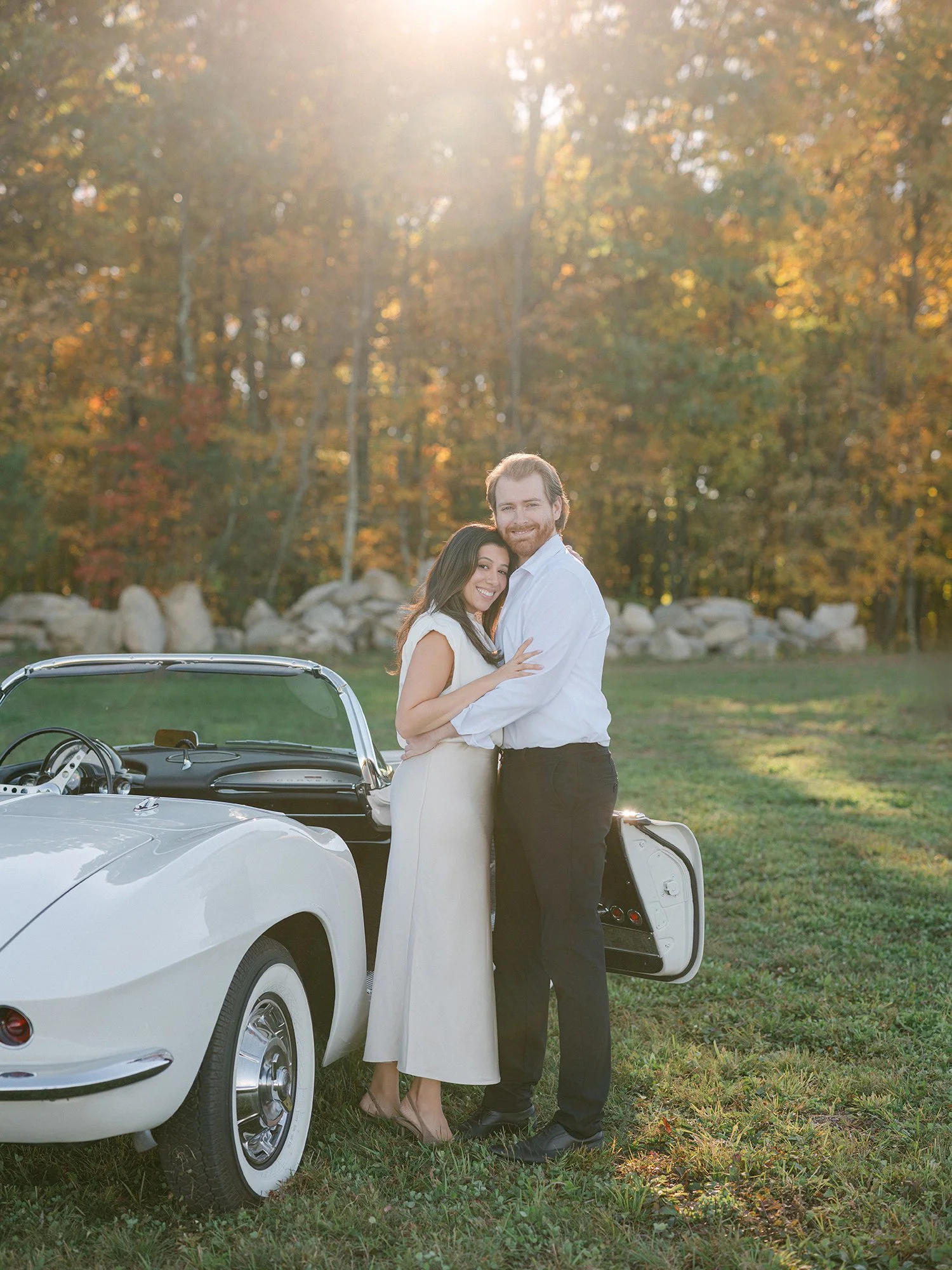 Daniel and Sandra beside a white 1960s Corvette convertible on a hill above the Hudson Valley
