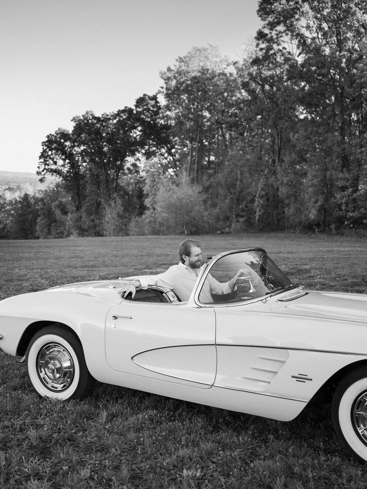 Daniel and Sandra in a white 1960s Corvette convertible on a hill above the Hudson Valley