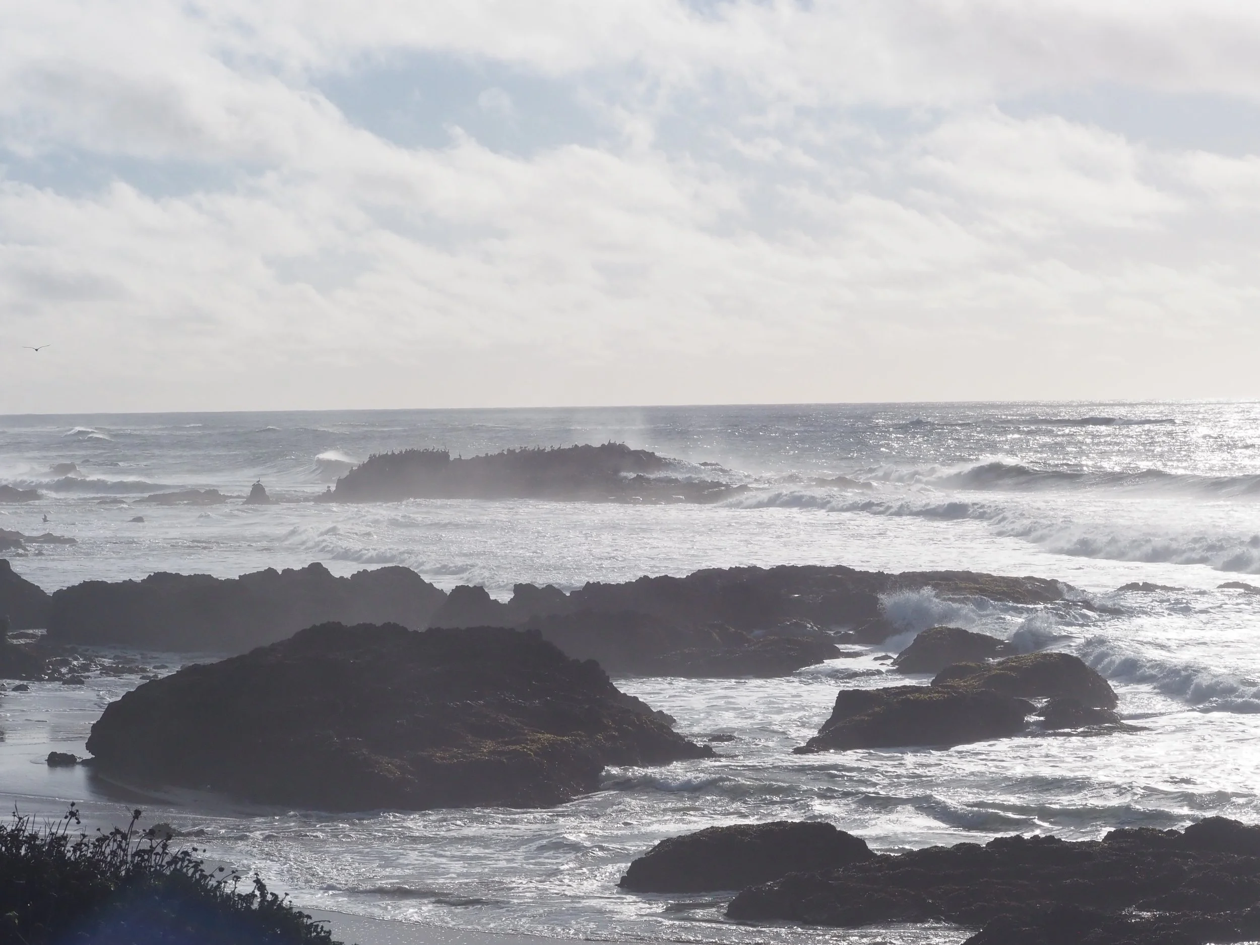 Rocky coastline with waves crashing against the shore under a cloudy sky.