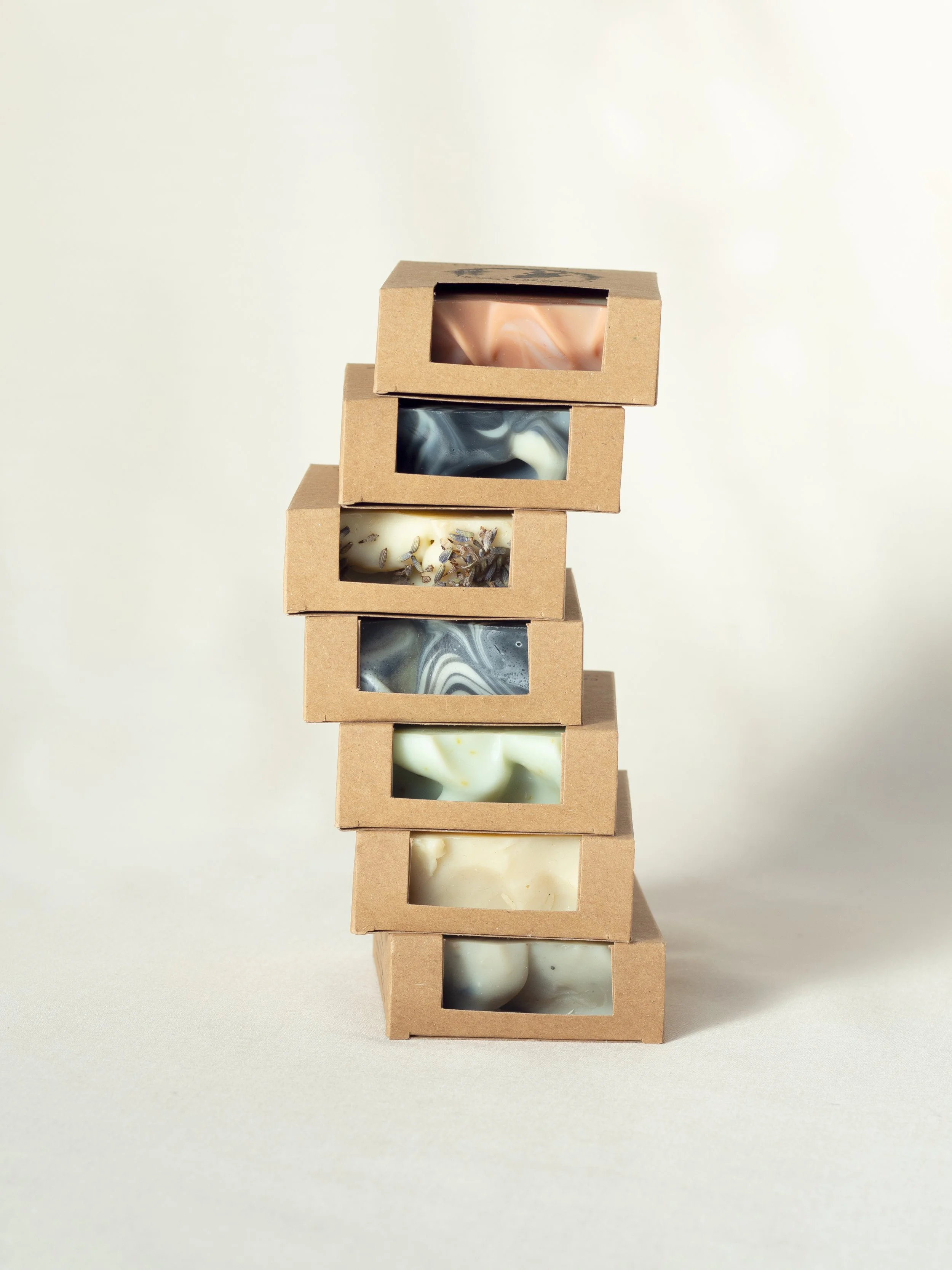Stack of natural soap bars in cardboard boxes with window openings, showcasing different colorful patterns.