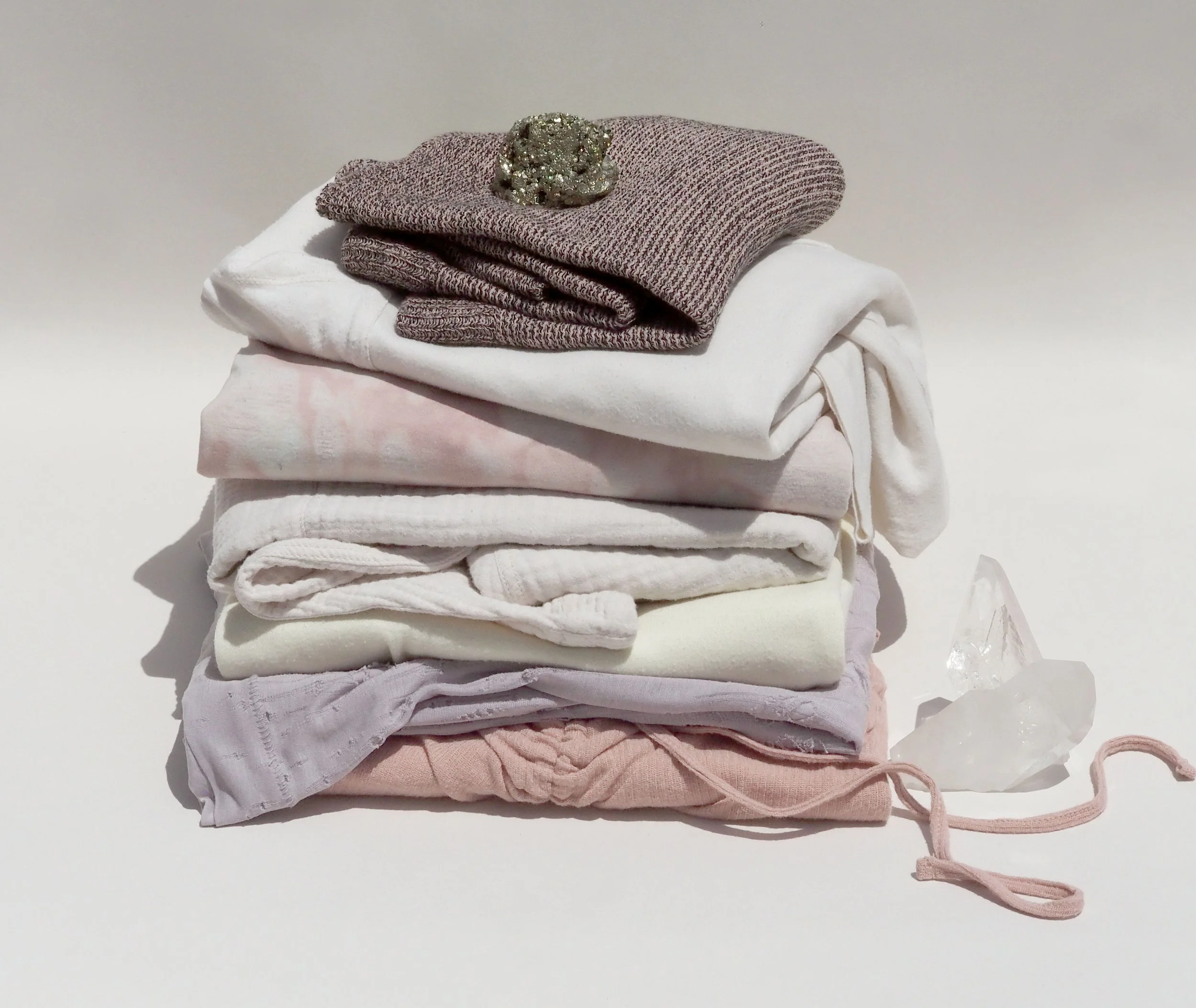 Stack of folded clothes in neutral tones with a wool hat on top and a crystal beside them
