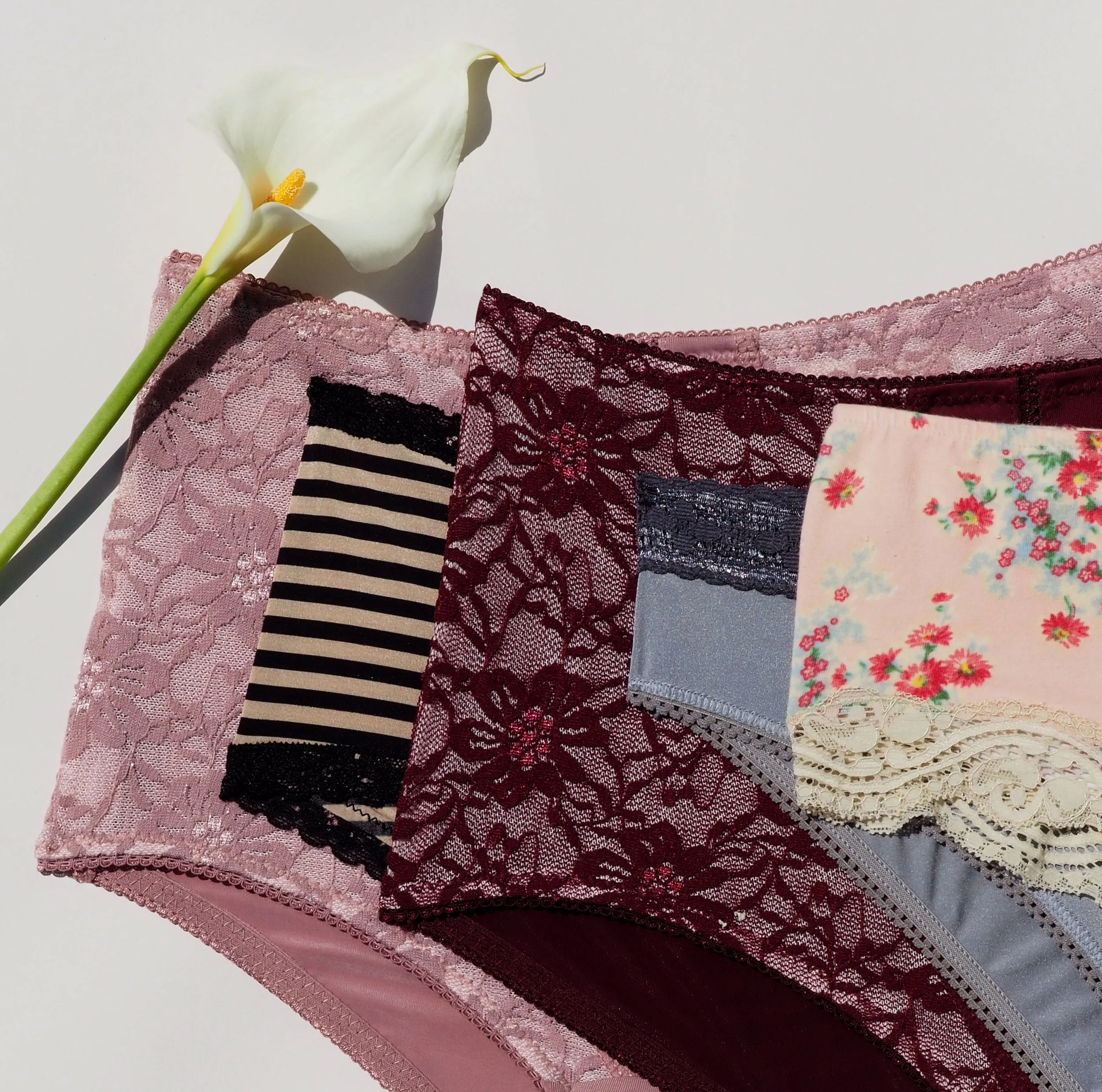 Assorted women's lace and patterned underwear with a white calla lily flower.