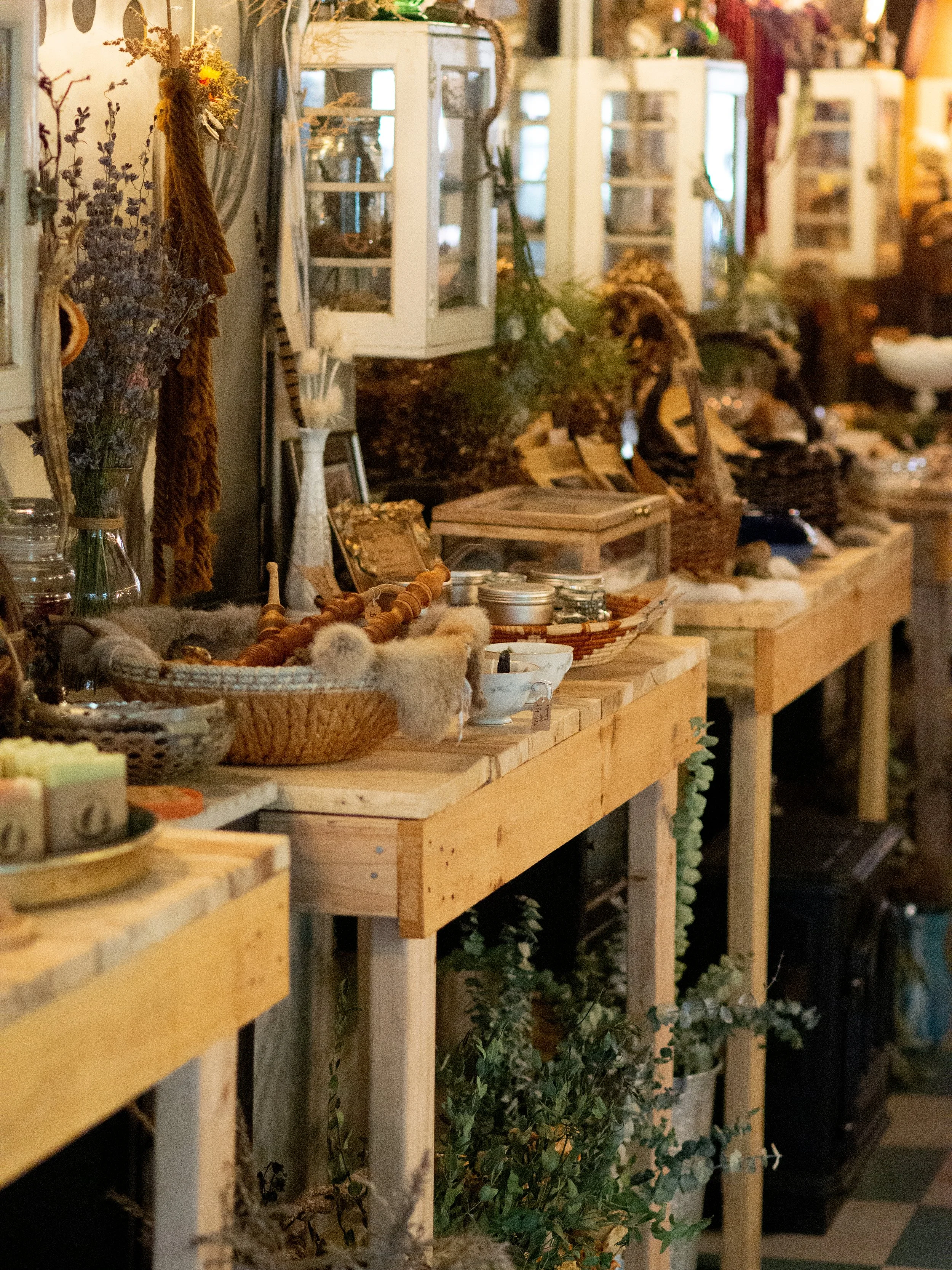 Assorted rustic decor and dried flowers on wooden tables in a vintage shop, with baskets, jars, and natural elements displayed.