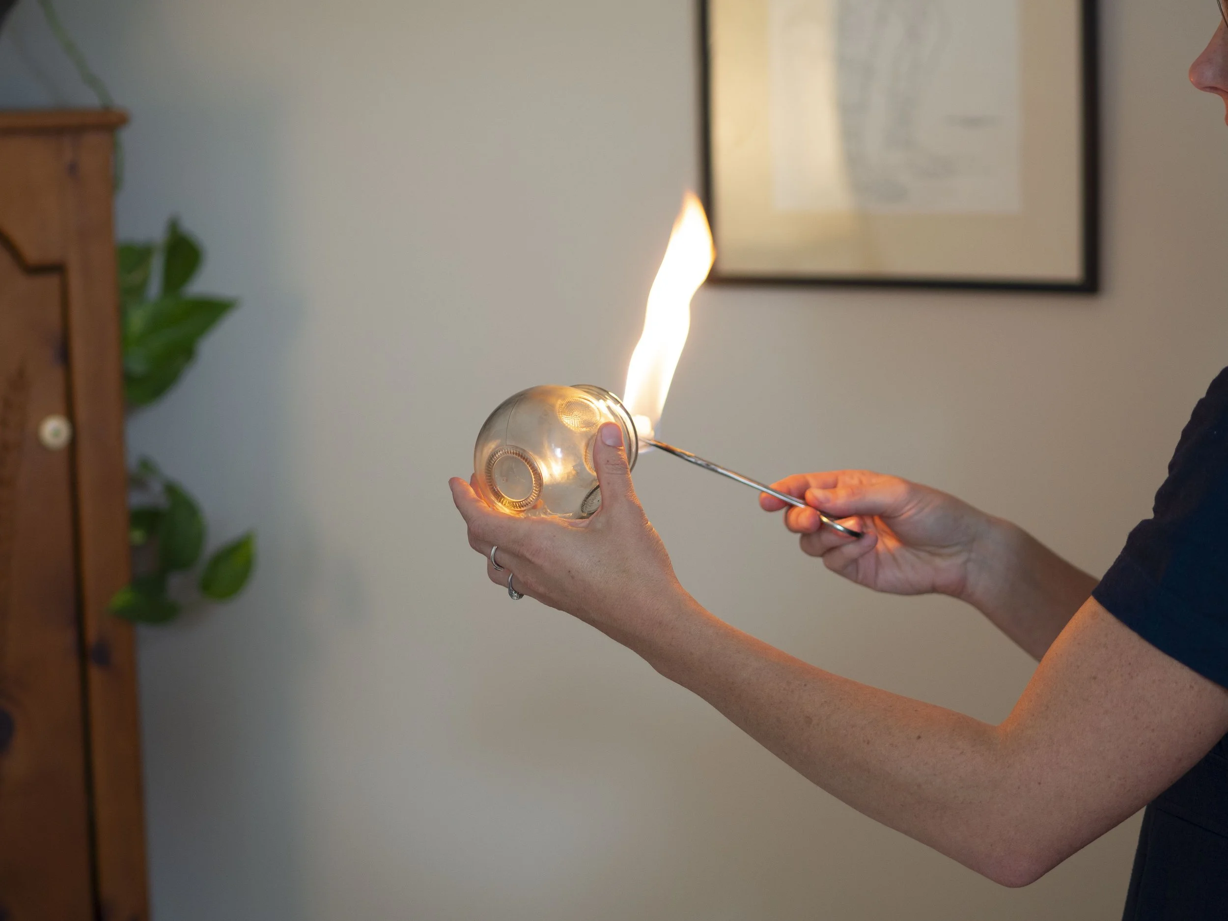 Person performing fire cupping therapy with a glass cup and a flame heated instrument in a wellness setting.