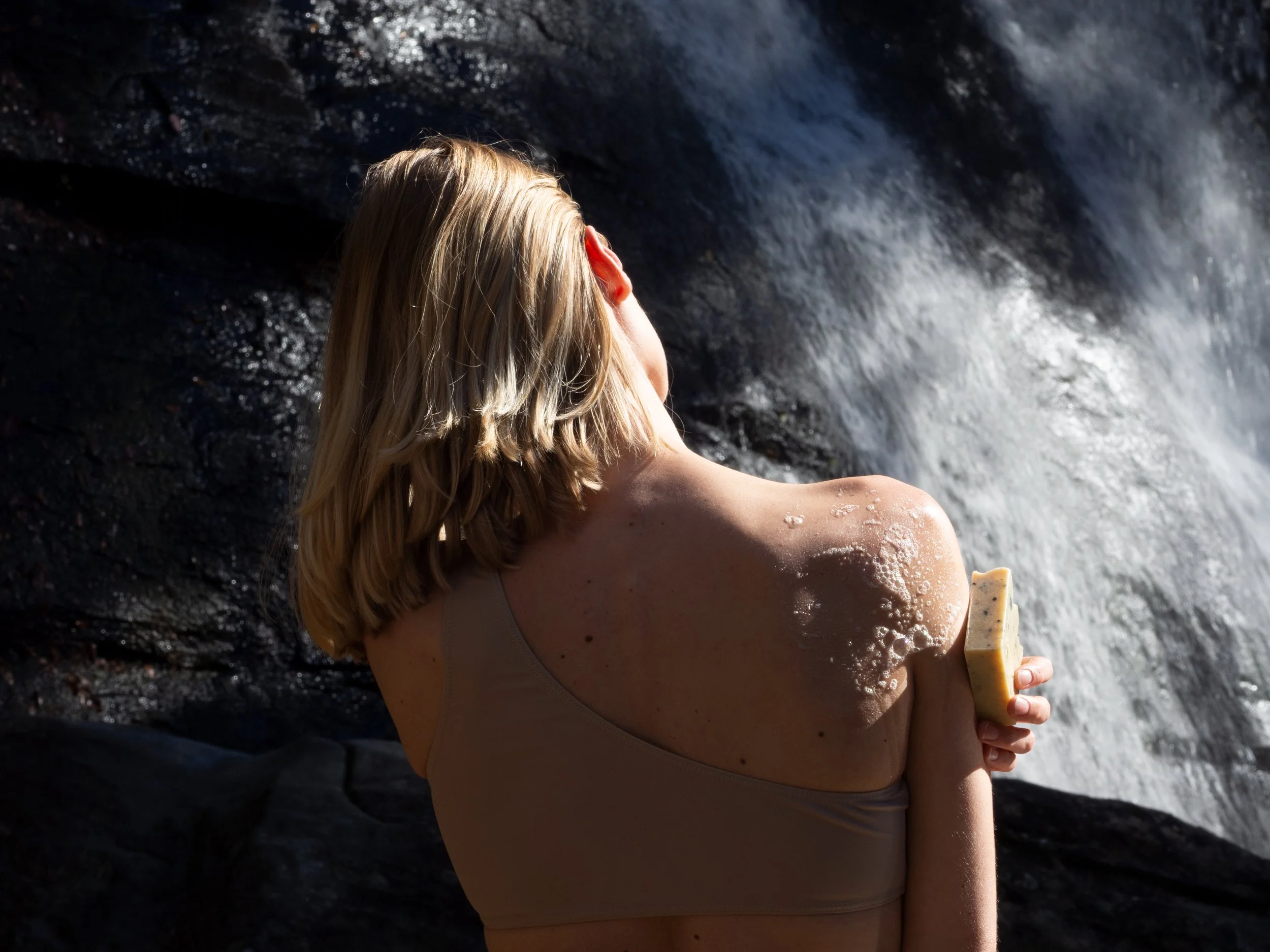 Person using soap on shoulder near waterfall