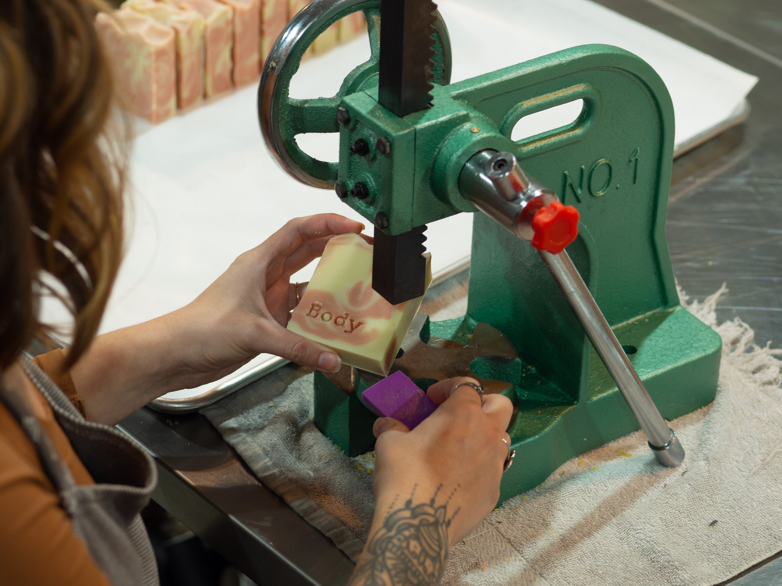 Person using a manual press to stamp a soap bar with the word 'Body'
