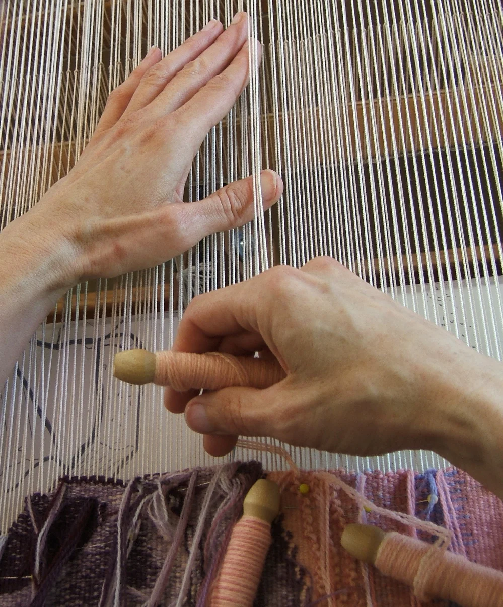 Elizabeth Buckley's hands weaving, with bobbins of crewel weight wool yarn. Photo credit: Lany Eila.