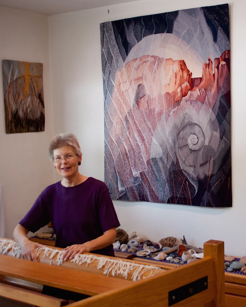 Elizabeth J. Buckley in her studio. Tapestries behind: The Veils of Time 60" x 50 ©2017 ; Fossil, Feather, and Light 25" x 18" ©2013 Photo credit: Nancy Wohlenberg