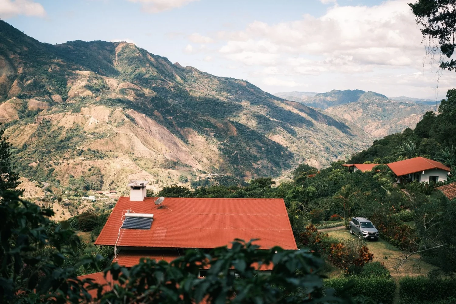 Red tin roofs of the La Minita farmhouse above a steep green valley