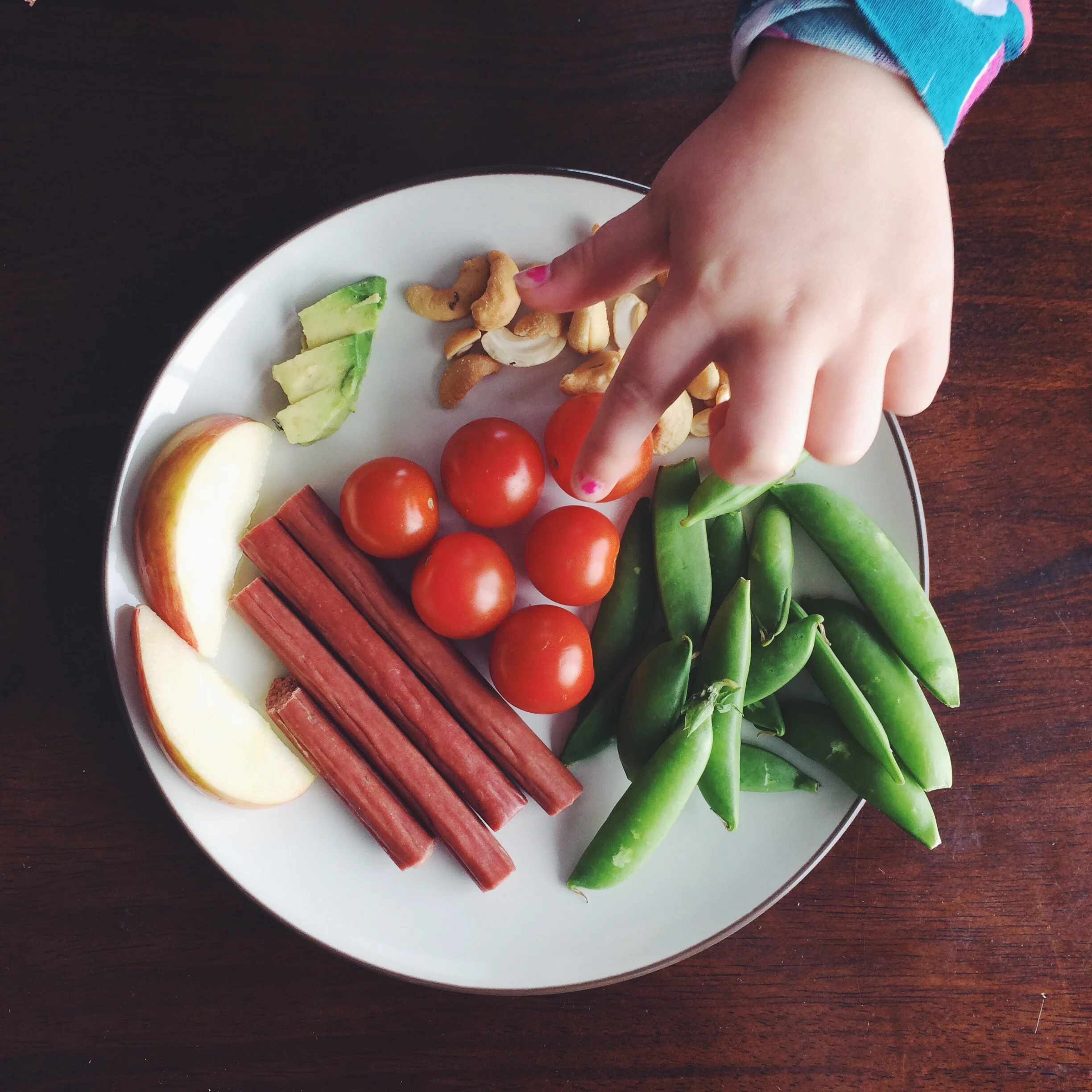 Grass-fed beef sticks, sugar snap peas, cherry tomatoes, apple slices, avocado slices and cashews.