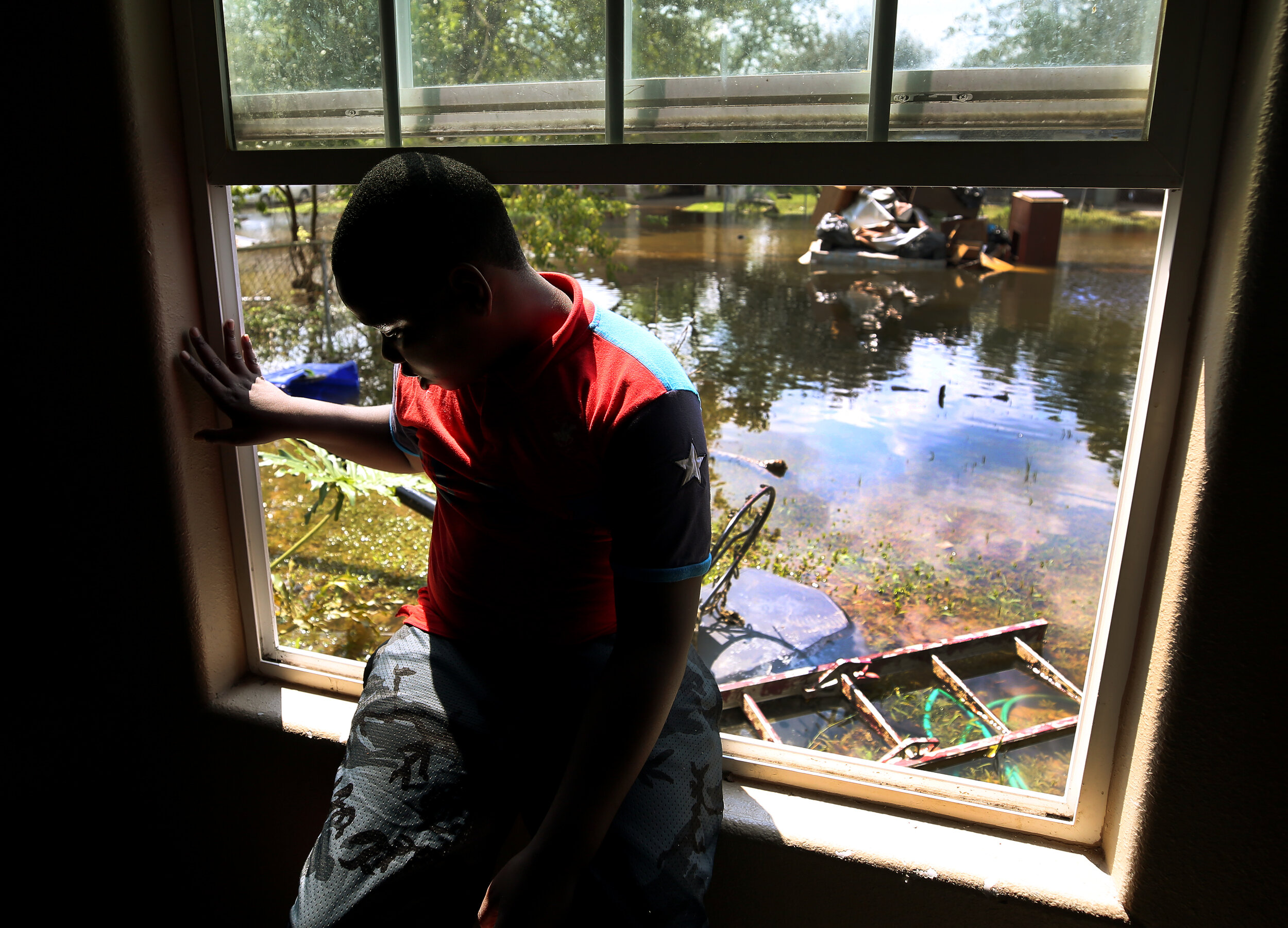  London Robinson, 9, sits on the windowsill of his room at his grandmother's home as the front yard remained flooded Sunday, Sept. 3, 2017, in Beaumont, Texas. The Robinsons got together to dispose of the destroyed flooring and belongings inside the 