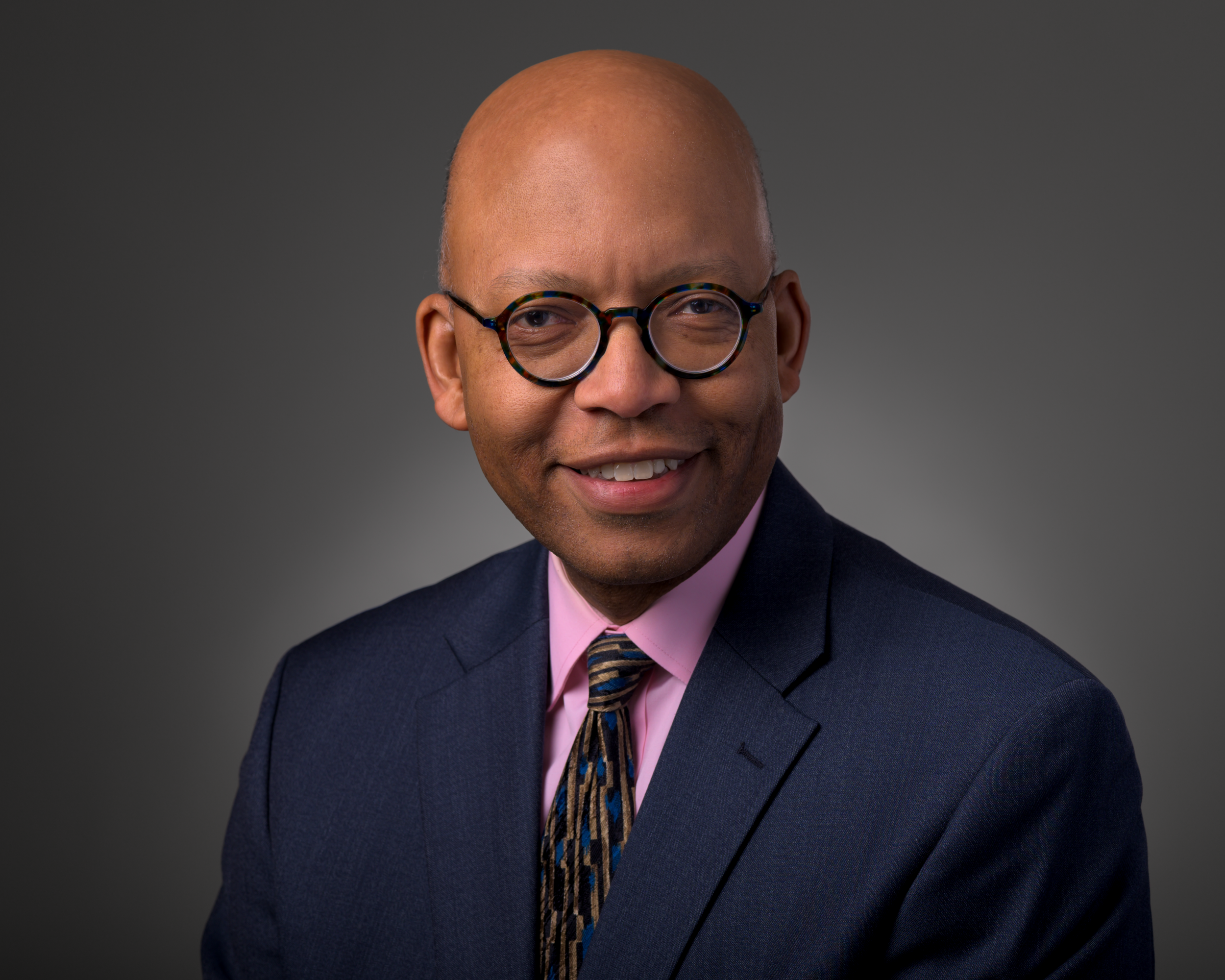 Professional executive headshot of a man in a blue suit against a grey background