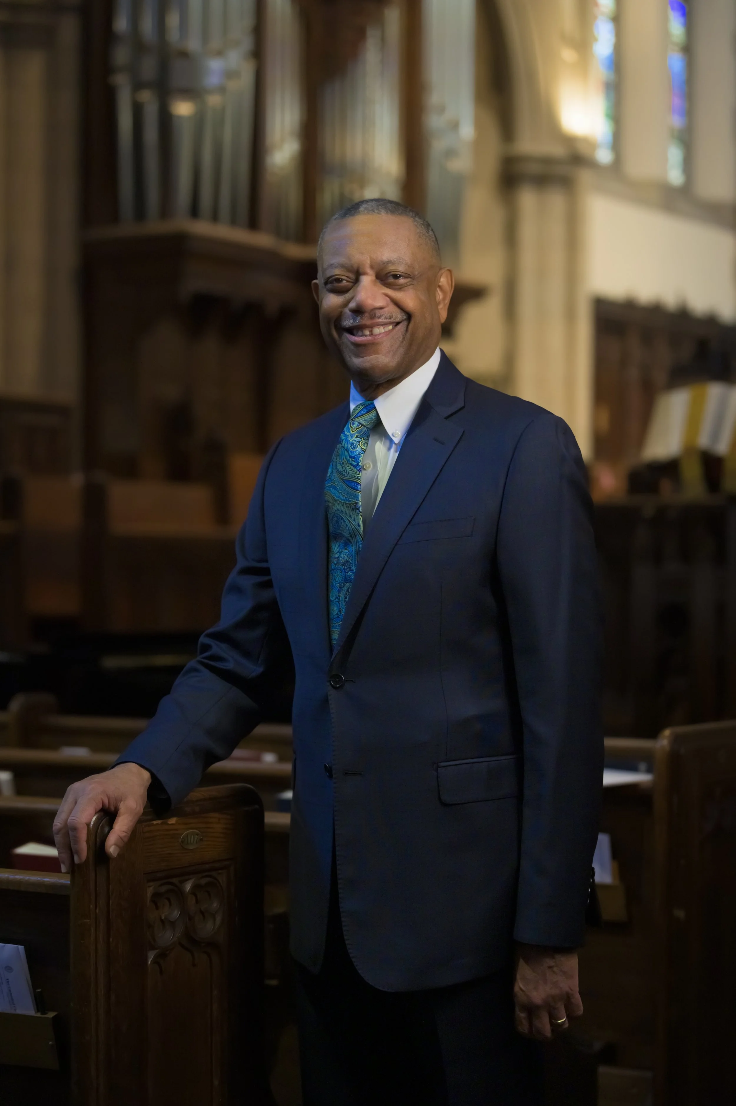 Environmental portrait of a man in a blue suit inside a church with a pipe organ in the background