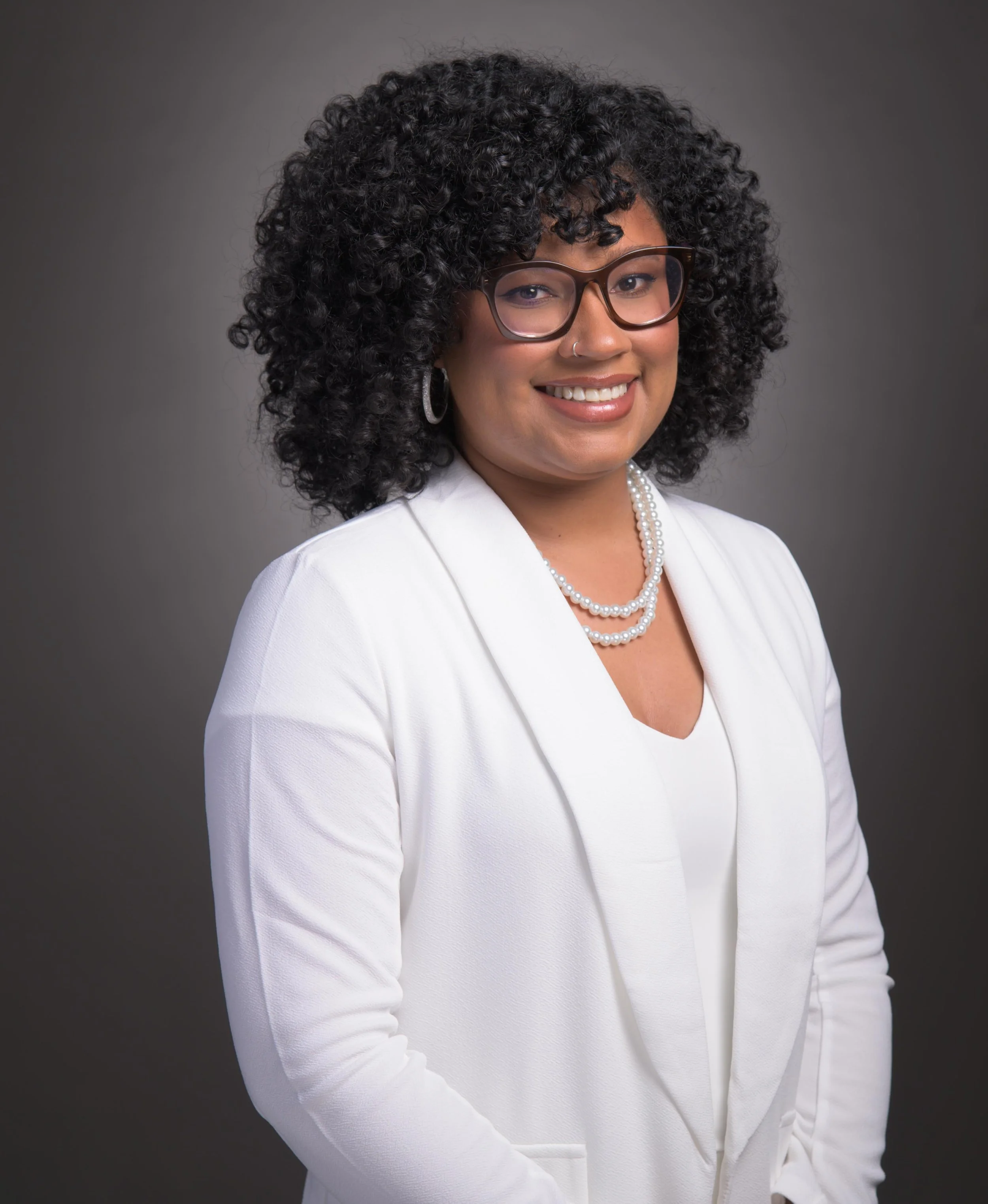 Professional portrait of a realtor in a white suit against a grey background