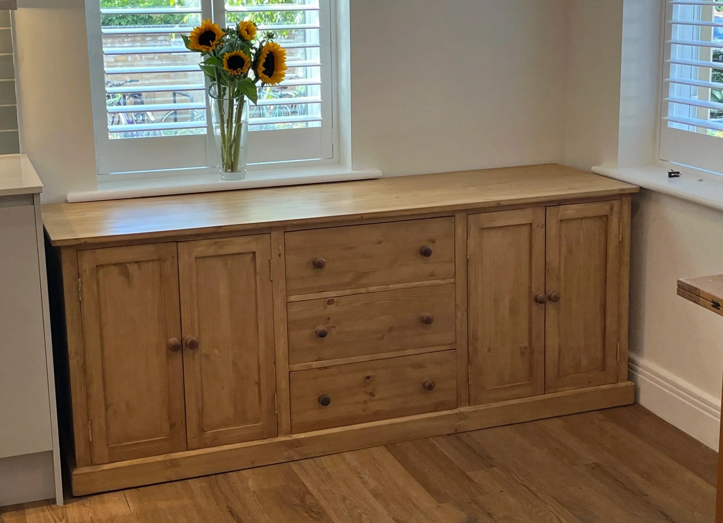 A large pine sideboard with 2 doors on each side, and a stack of 3 central drawers, all made to size from new pine, waxed in a light wax finish