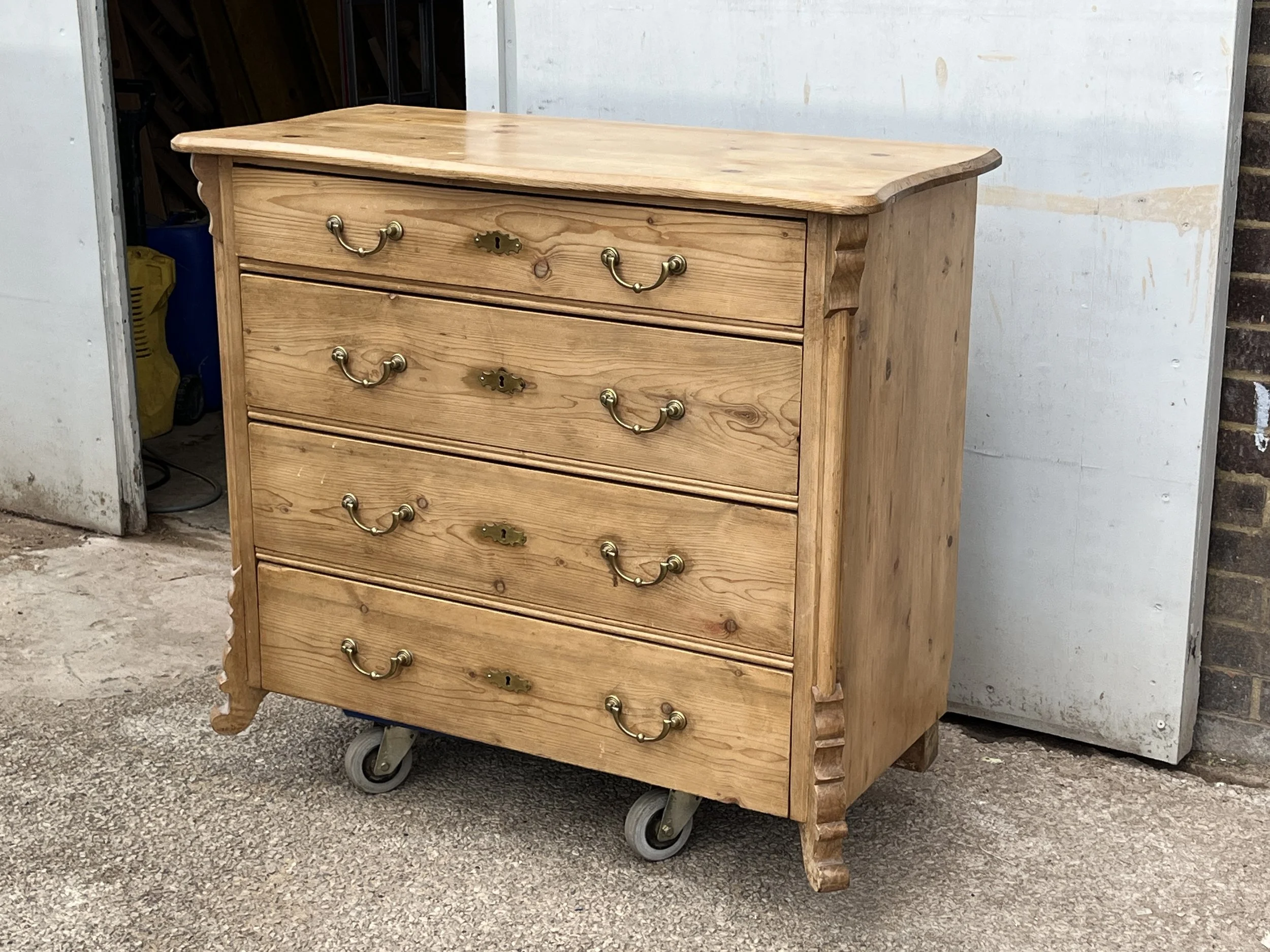 Angled front view of the continental pine chest with four full-width drawers and brass drop handles
