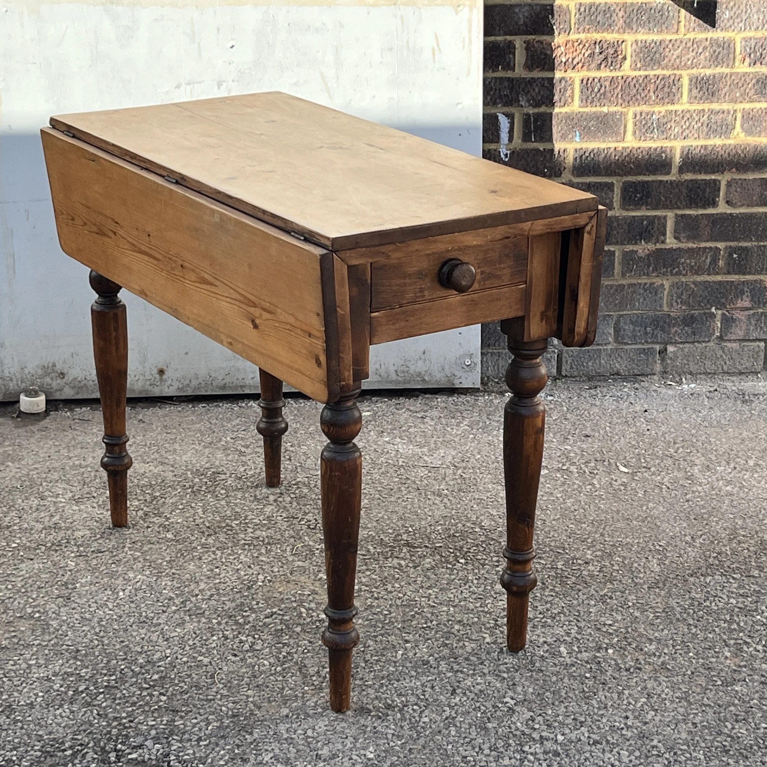 Pine drop-leaf table with leaves lowered, turned legs and an end drawer