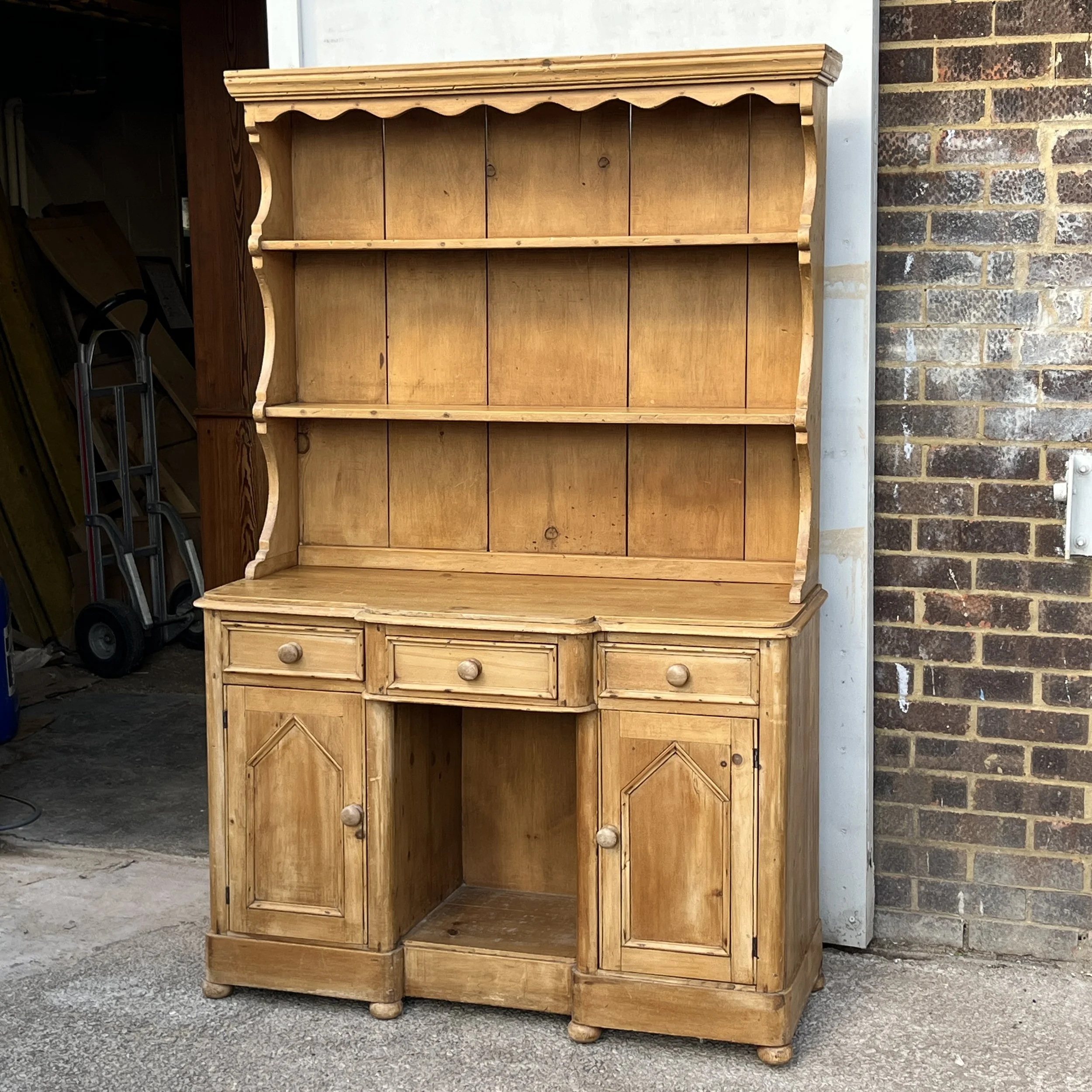 Small pine dresser with open shelf rack, three drawers and cupboard doors around an open central recess