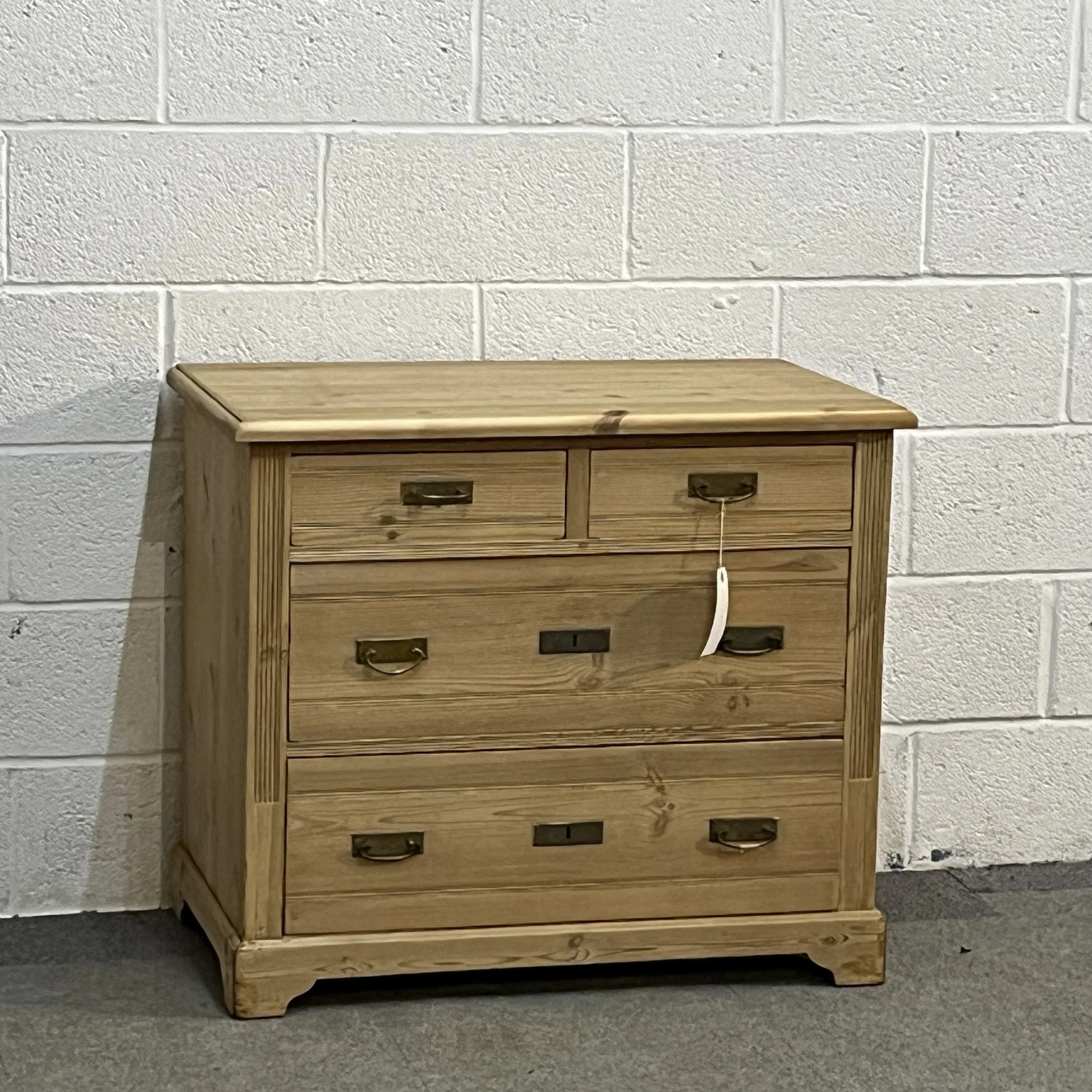 Small 1930s pine chest of drawers N8004C, full front view from the left with brass drop handles and bracket feet.