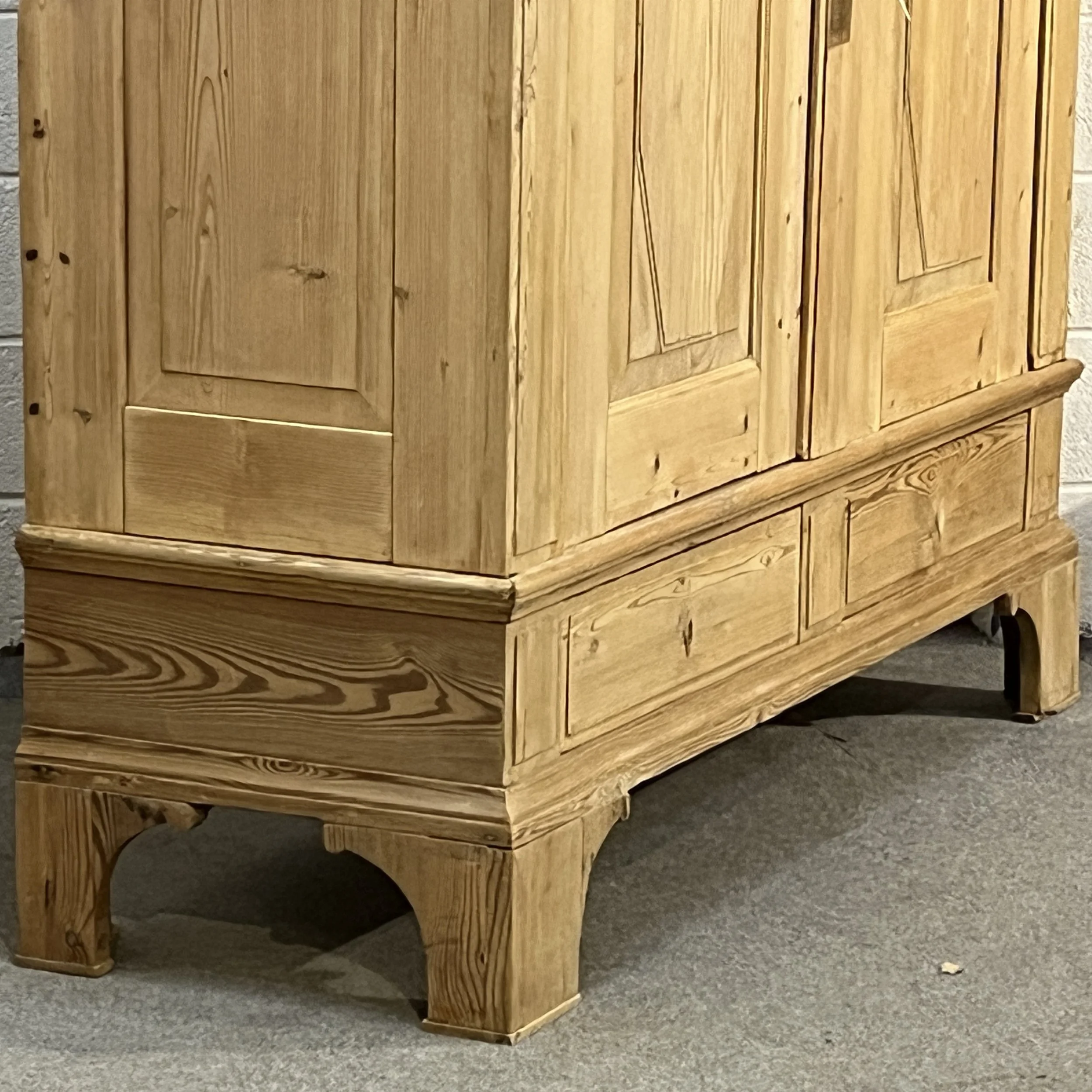 Lower left corner of pine wardrobe N8206H showing panelled base, drawer fronts and high bracket feet.