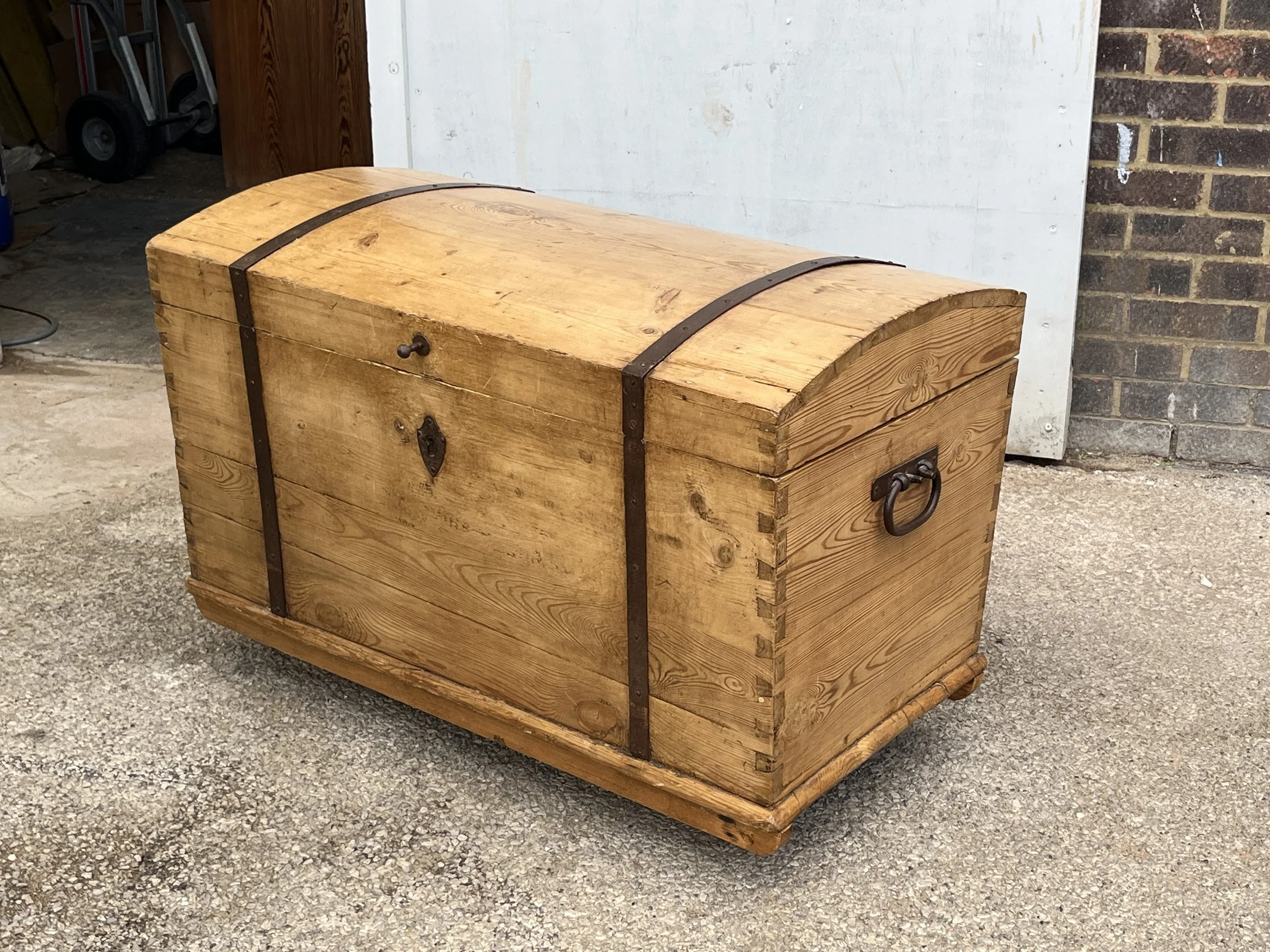 Angled view of the old pine dome-top blanket chest showing metal straps and an end carrying handle