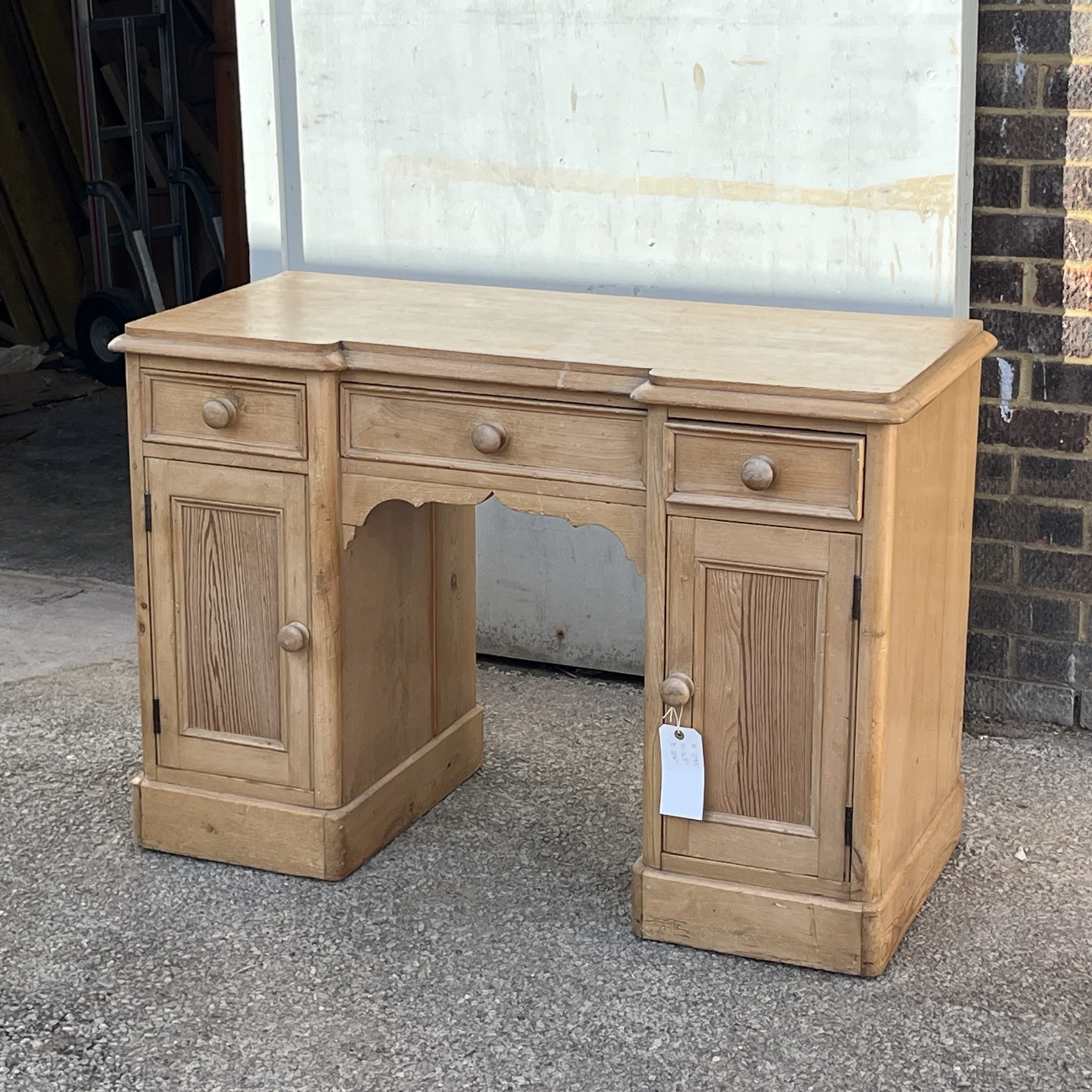 Angled front view of the pine pedestal desk with three upper drawers and two panelled cupboard doors