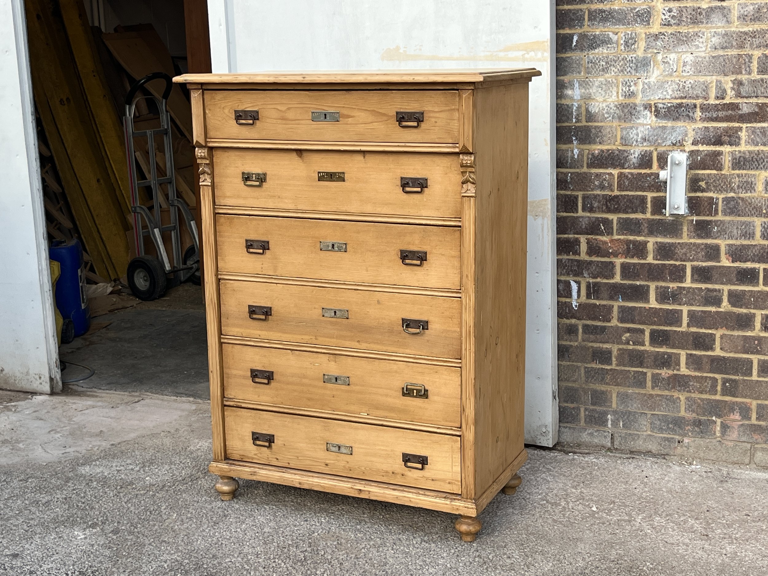 Angled front view of the tall pine chest with six drawers and metal drop handles