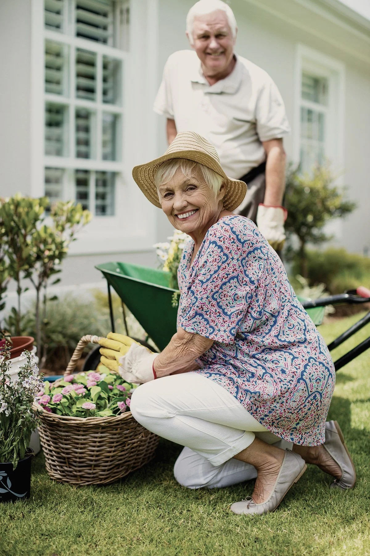 A smiling older woman in a sun hat planting flowers in her garden.