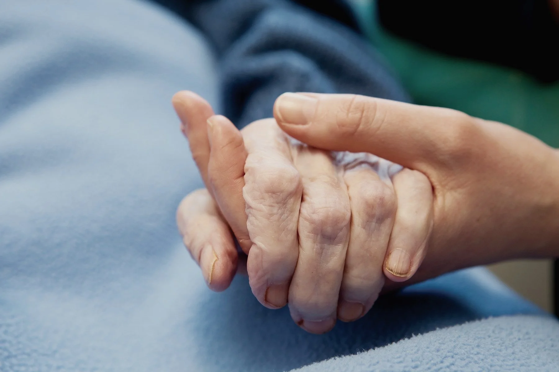 A younger hand gently holding an older person's hand on a soft blue blanket.