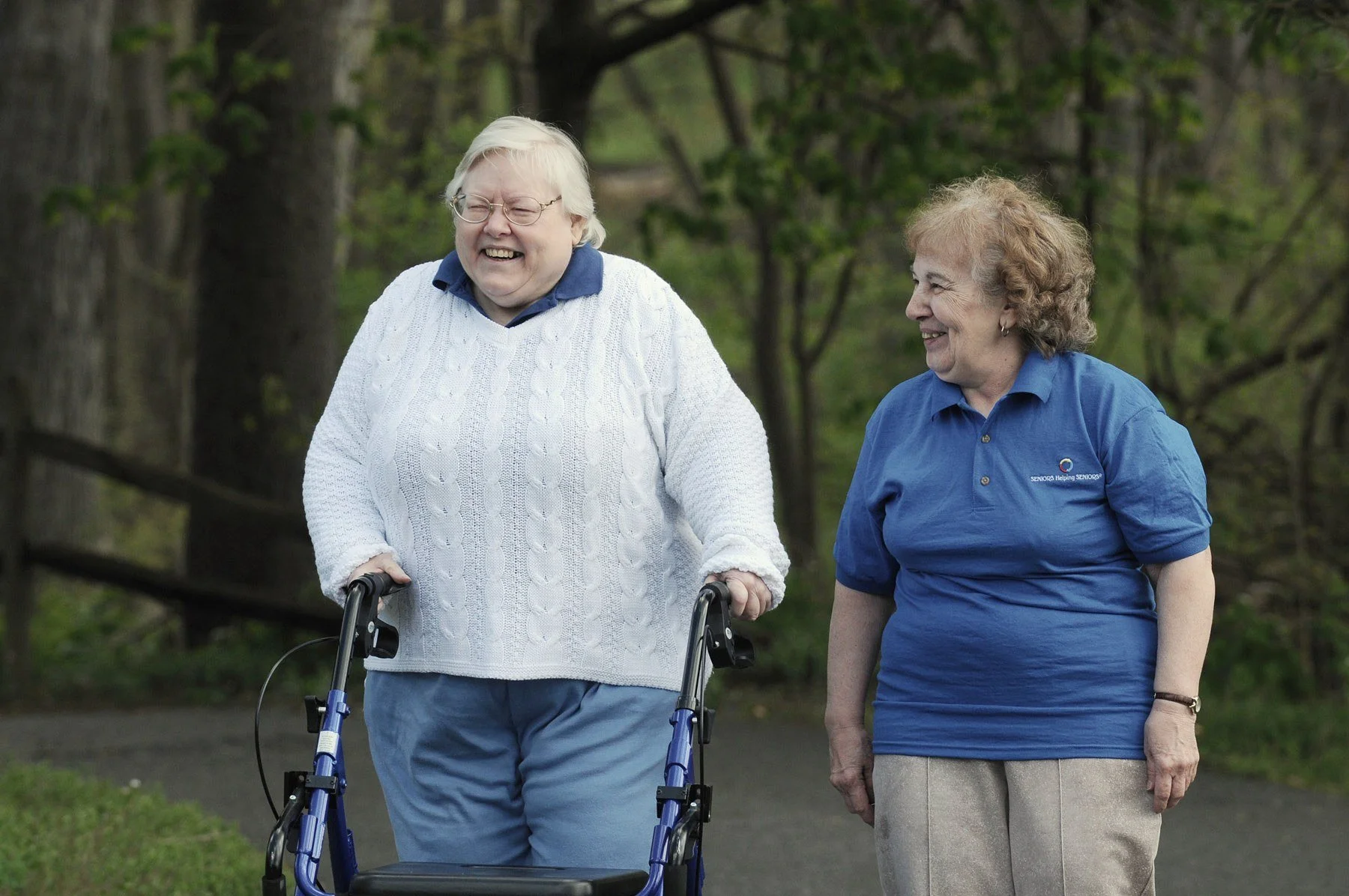 Two older women laughing together on a walk outdoors.