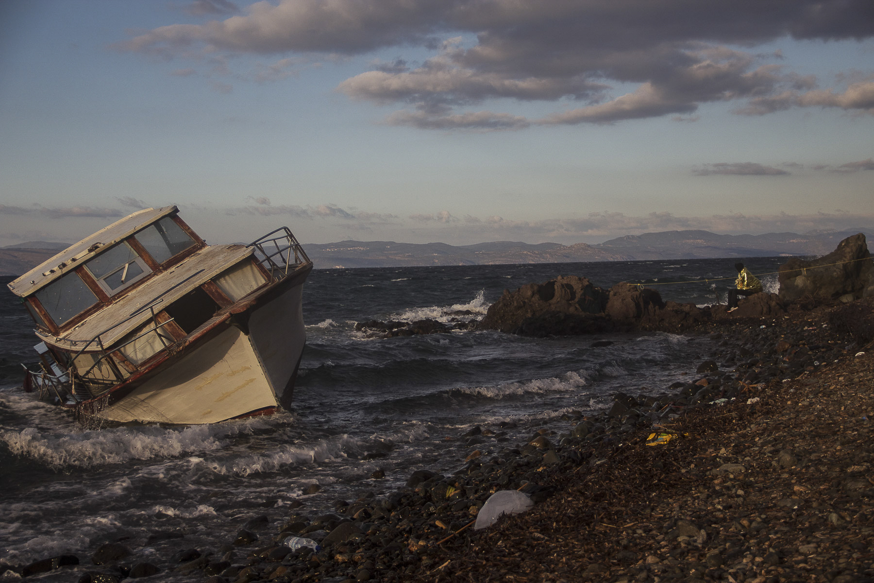   A refugee sits looking out at the boat he and dozens of others used to cross the Aegean from Turkey just momenta before. October 2015.  