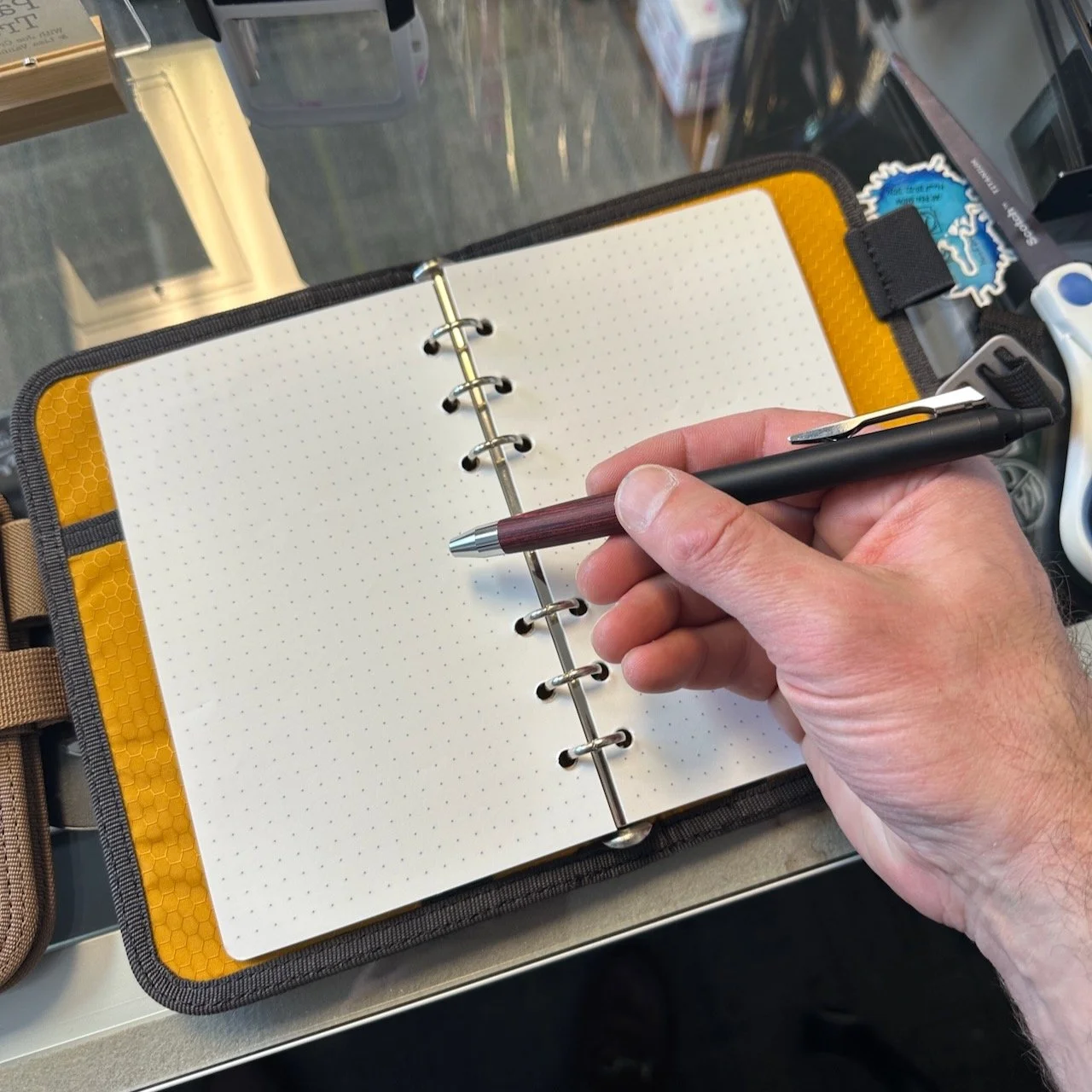 Lochby Field Binder A6 in Charcoal, shown with a pen and hand for scale