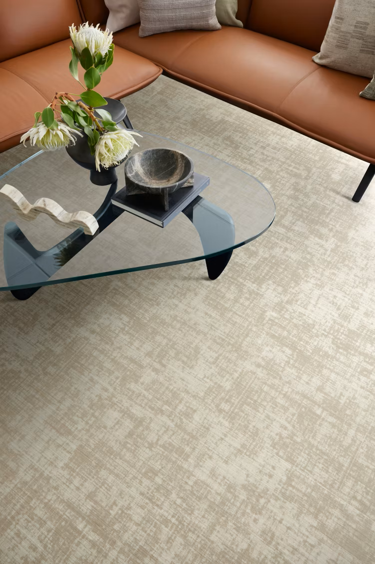 cream carpet installed under a glass table and tan leather sofa