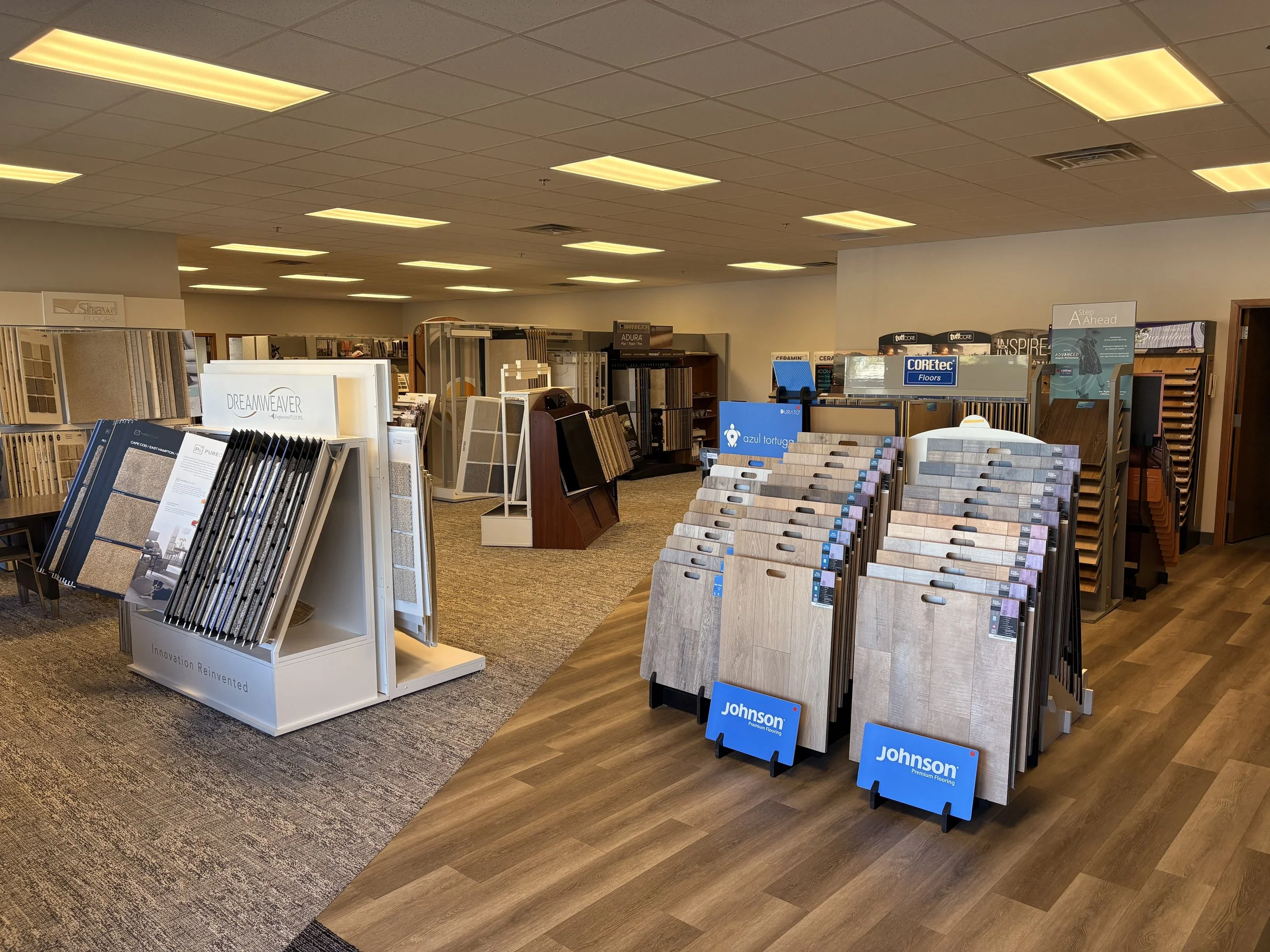 Interior of a flooring store displaying various samples of tiles, wood, and laminate flooring on display stands and shelving units.