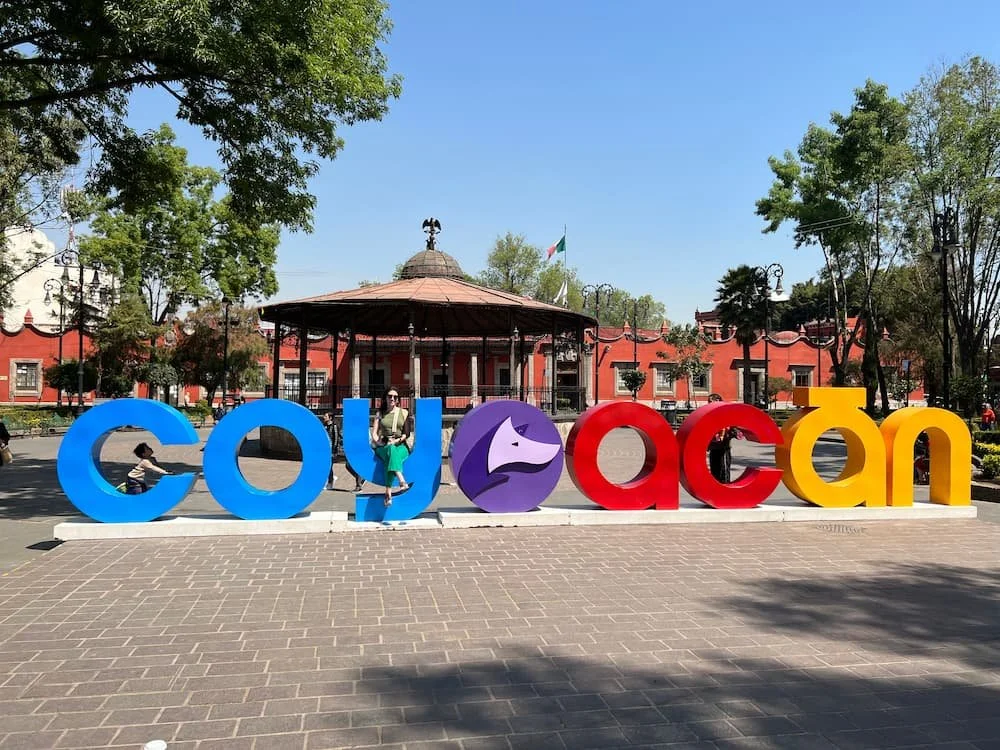 Colorful Coyoacán sign in a plaza with a gazebo and trees in the background in Mexico City