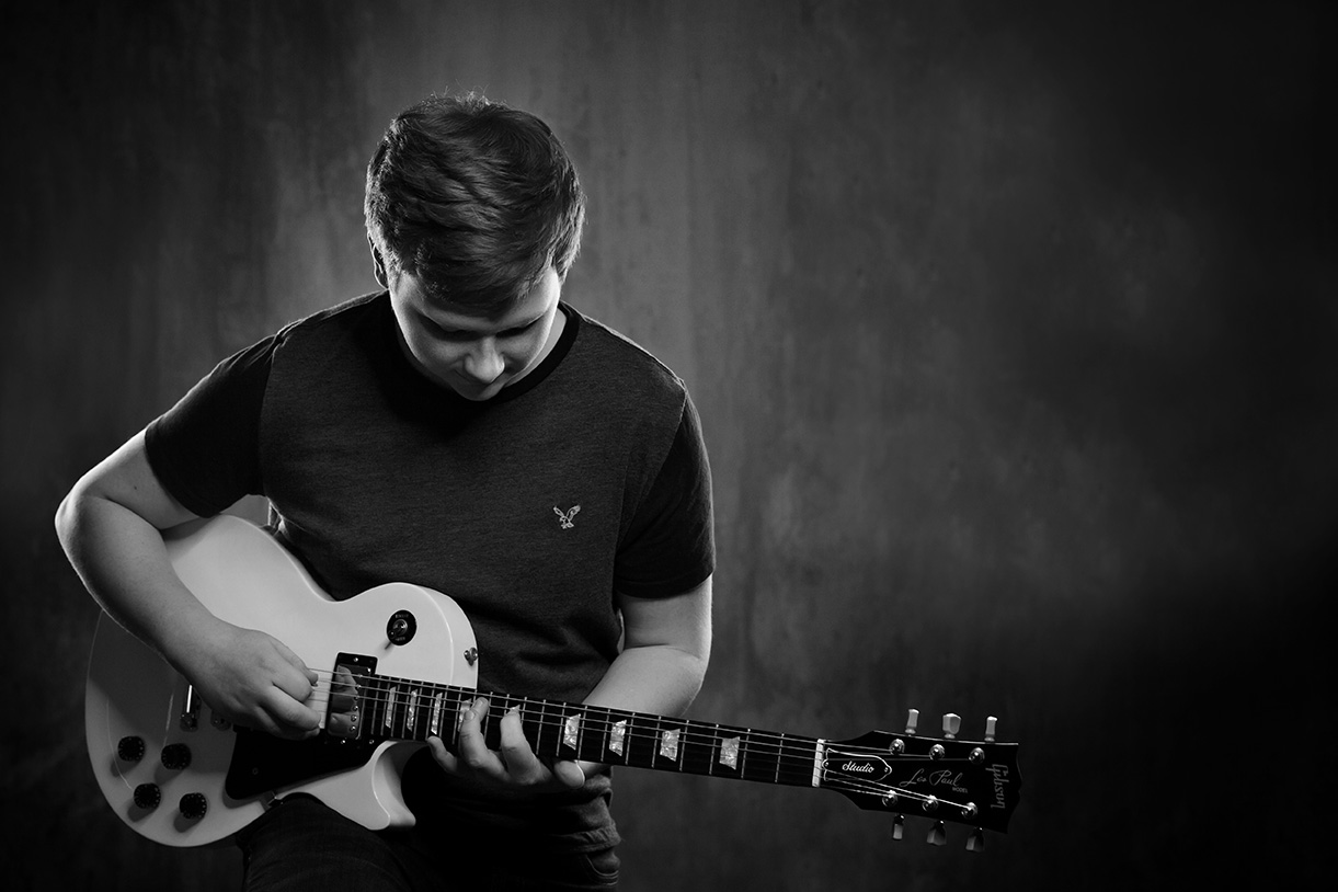 black and white photo of a senior guy playing a Les Paul guitar in-studio grungy background in Fredericksburg, Ohio